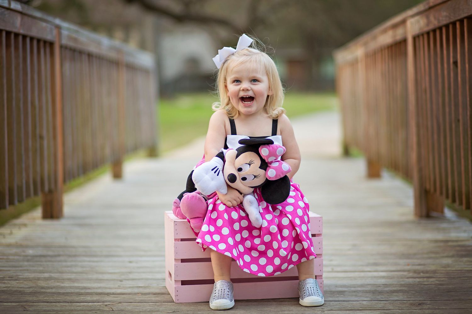 A child in pink Minnie Mouse attire poses on a wooden bridge outdoors.