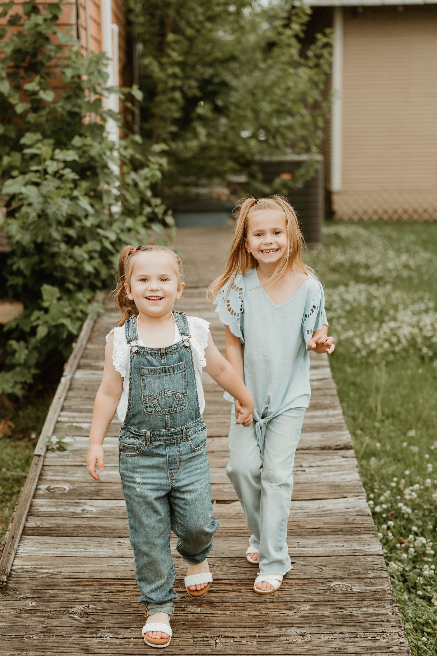 Children in denim overalls play and laugh while walking on a wooden boardwalk.