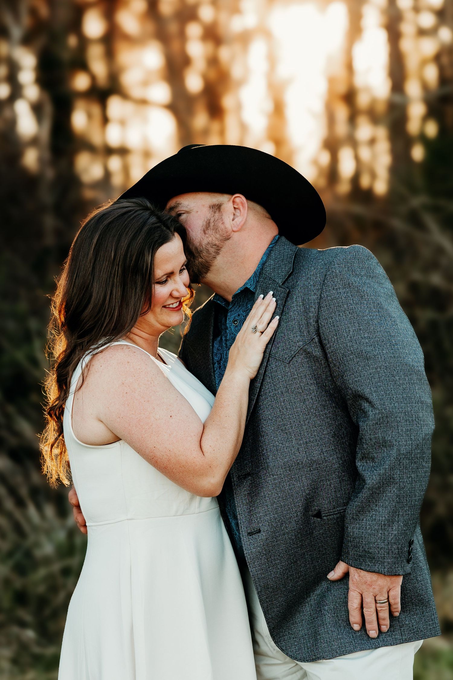 Romantic couple embraces during golden hour sunset photoshoot in a forest setting.