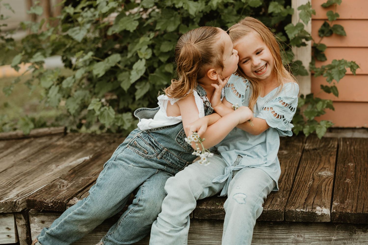 Two people share a sweet moment together on a wooden deck near a peach-colored building.