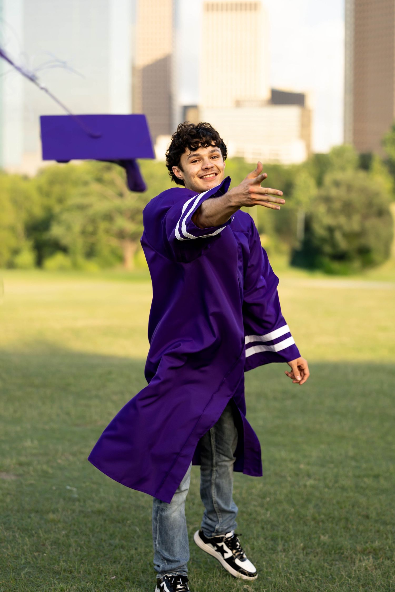 Person wearing a purple graduation gown spins joyfully on a grassy field.
