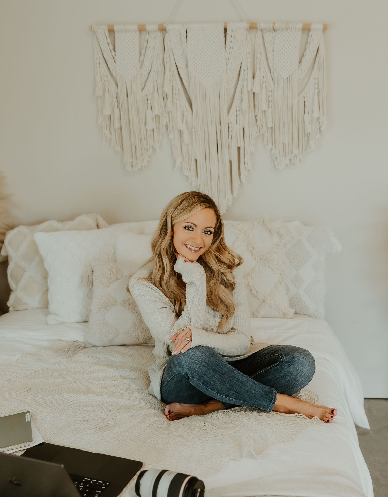 Person relaxing on white bedding with decorative wall hangings and neutral decor in a cozy bedroom setting.