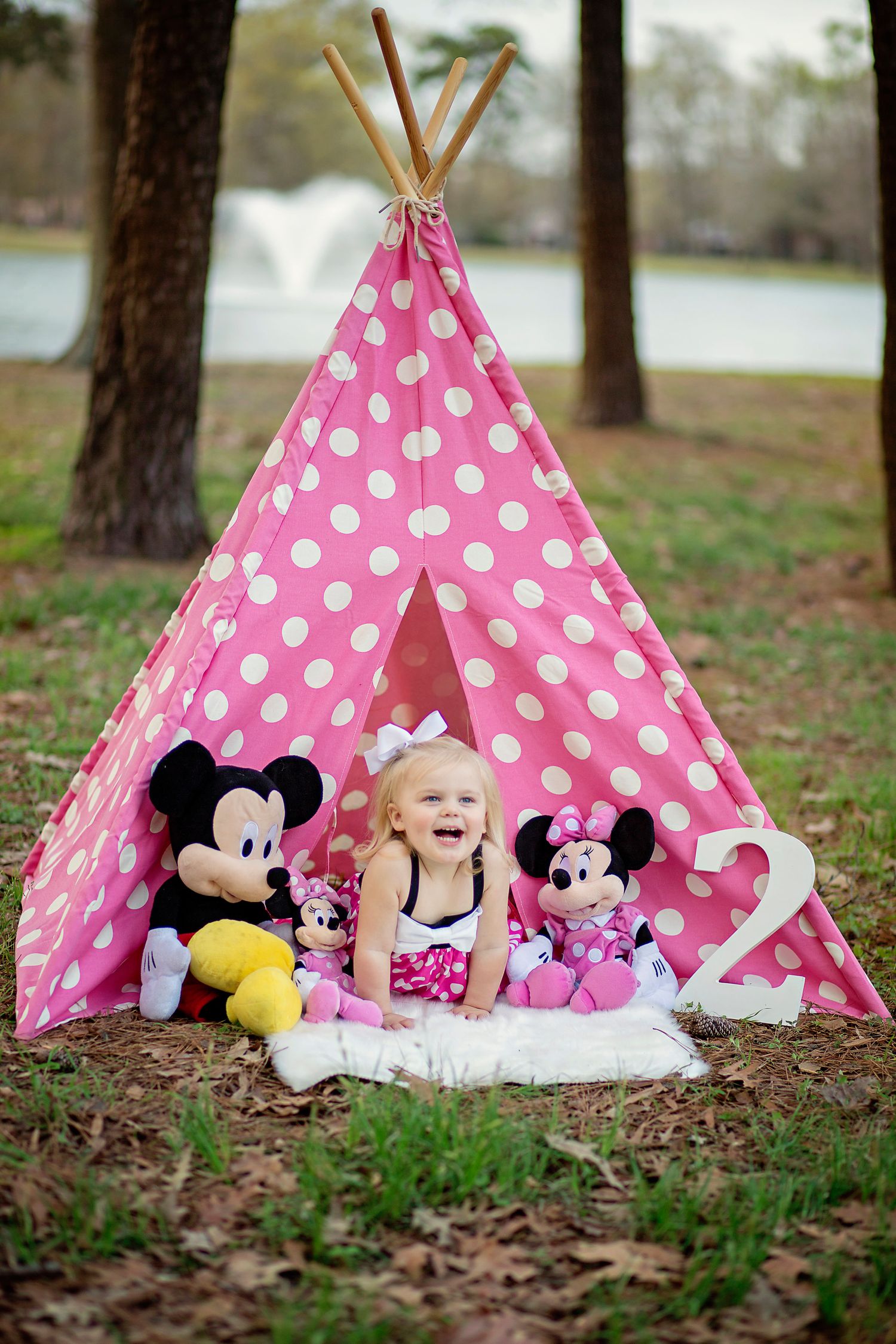 A pink polka dot teepee tent with Disney plush toys and white bedding set up outdoors.