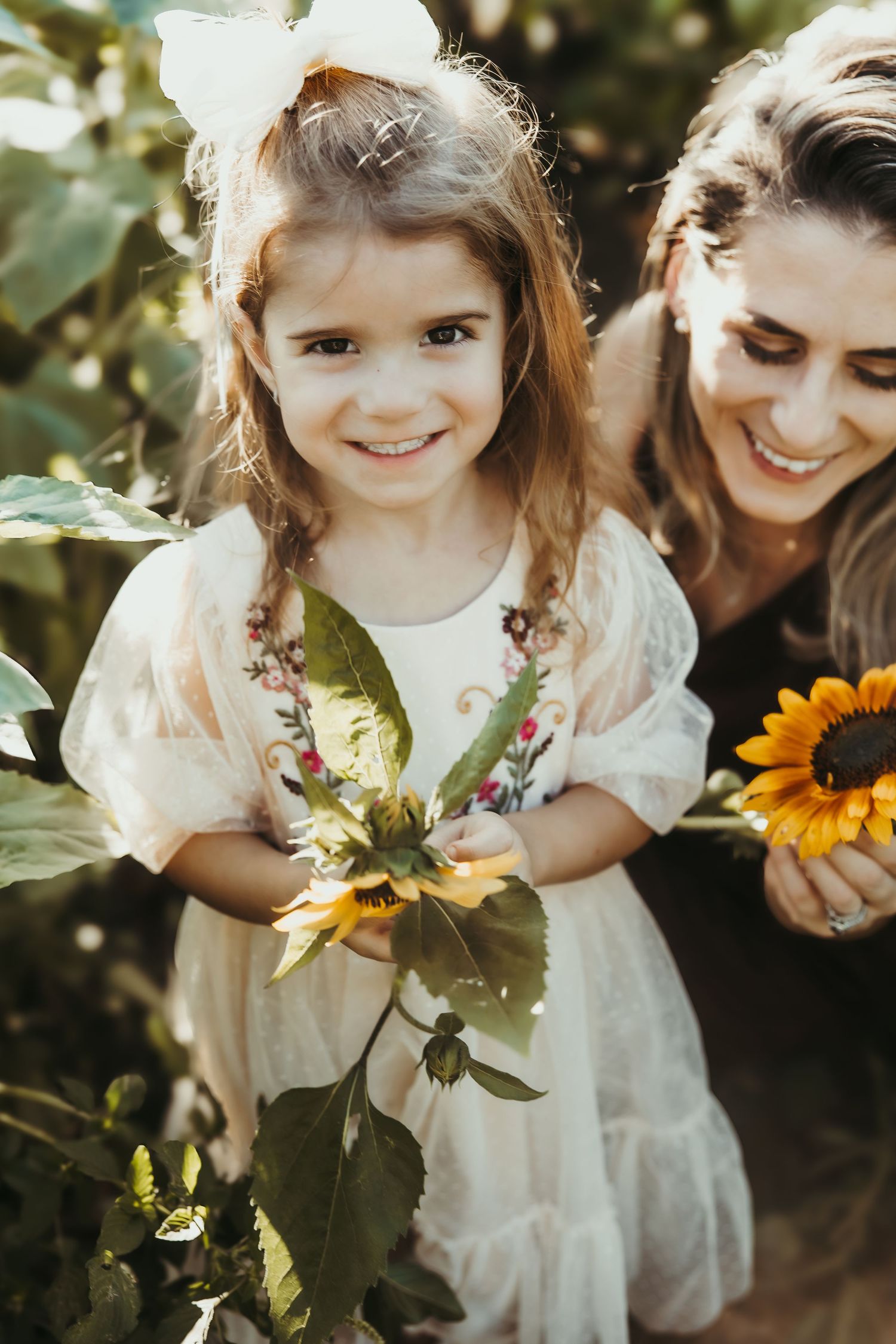 Sweet interactions among sunflowers with white lace dress details and natural sunlit backdrop.