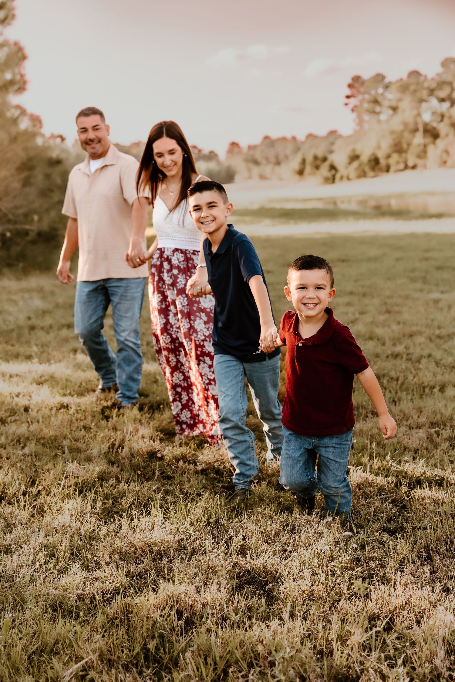 A family walks in a line through a grassy field during sunset photography session.