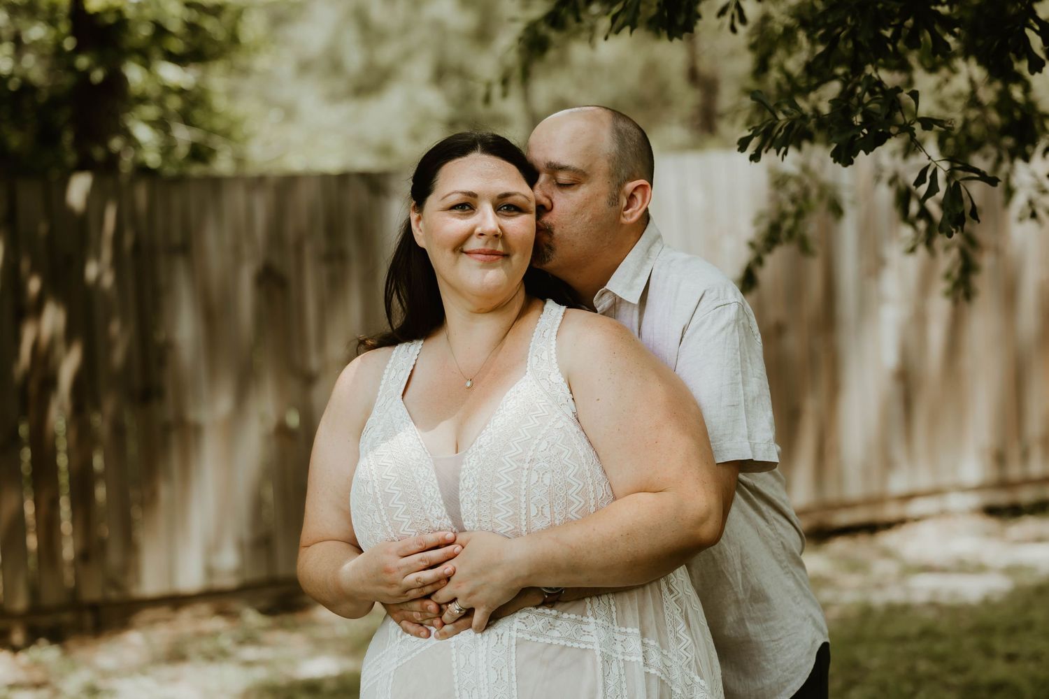 A couple dances and embraces in a backyard setting wearing matching white outfits.