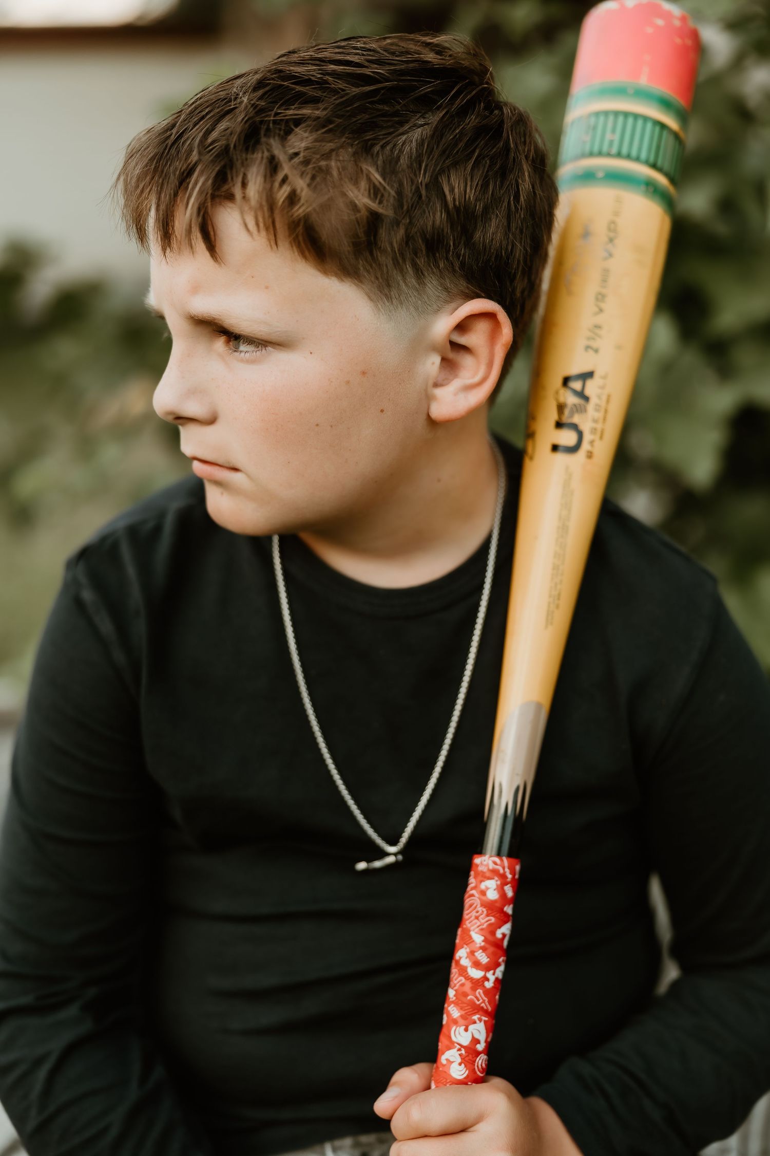 Youth in black sweater poses with wooden baseball bat in outdoor setting.