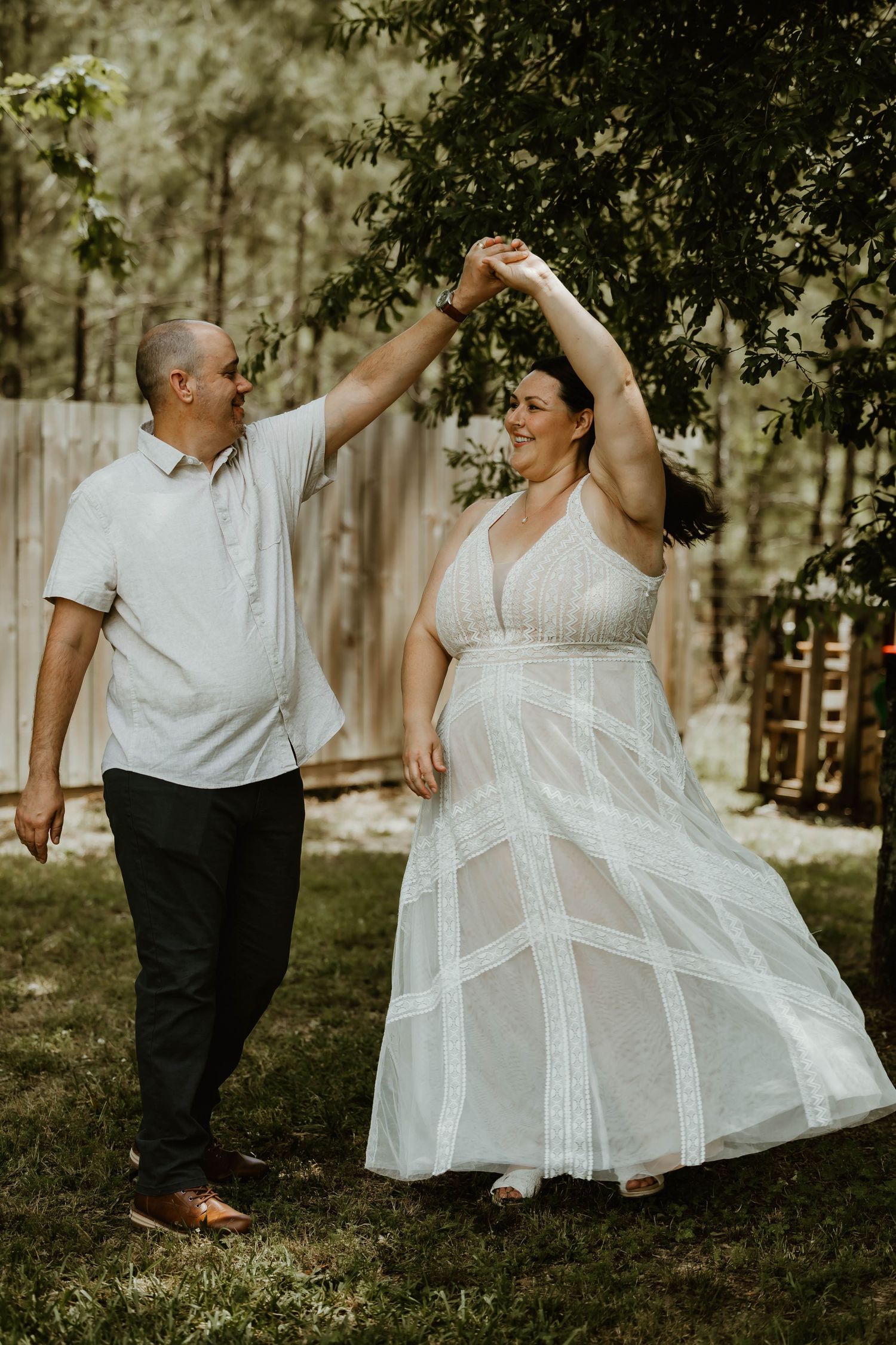 A couple dances playfully in a garden setting, with the woman's white dress flowing in motion.
