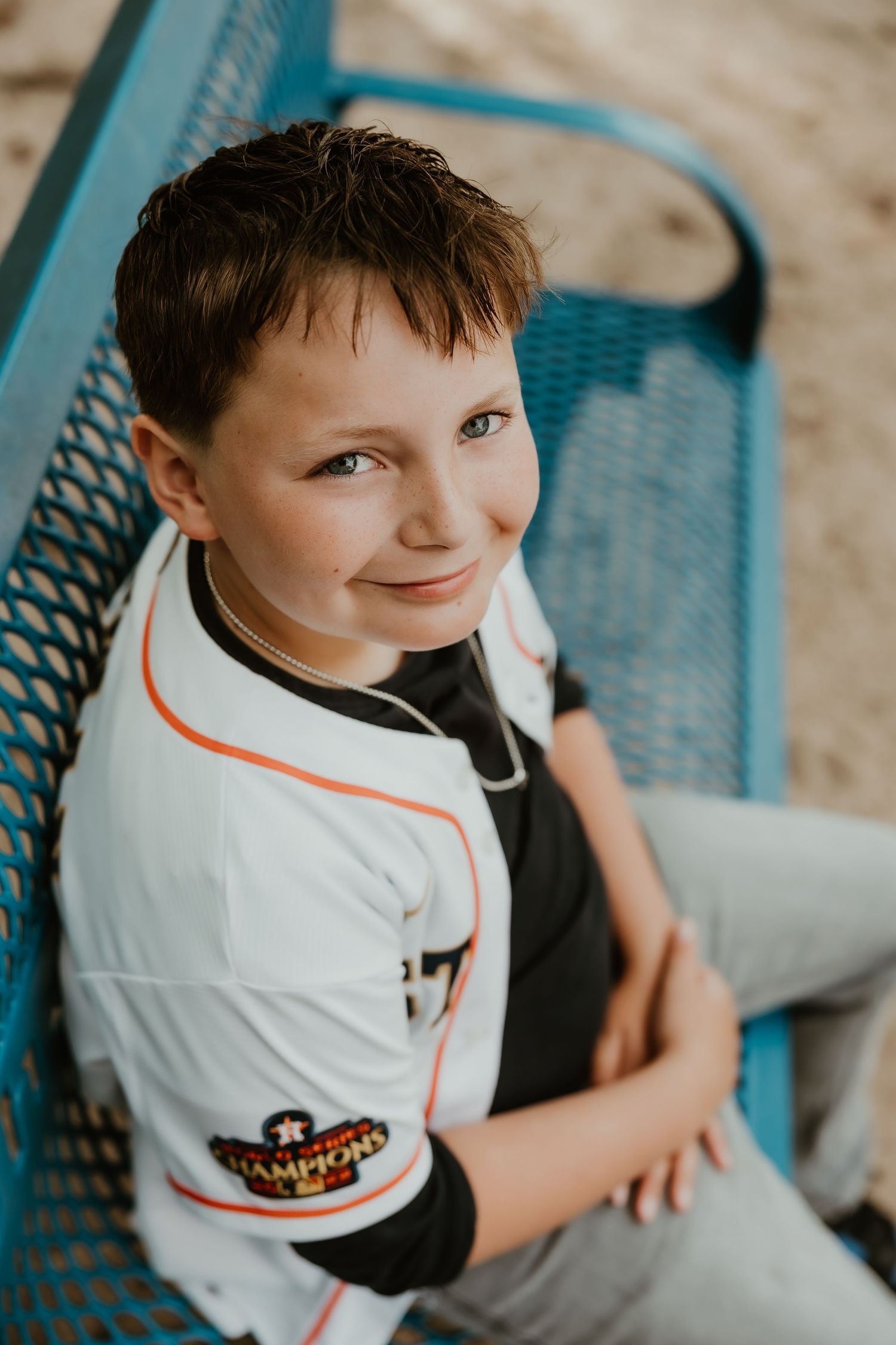 Young sports fan wearing a white baseball jersey sits in a turquoise chair.
