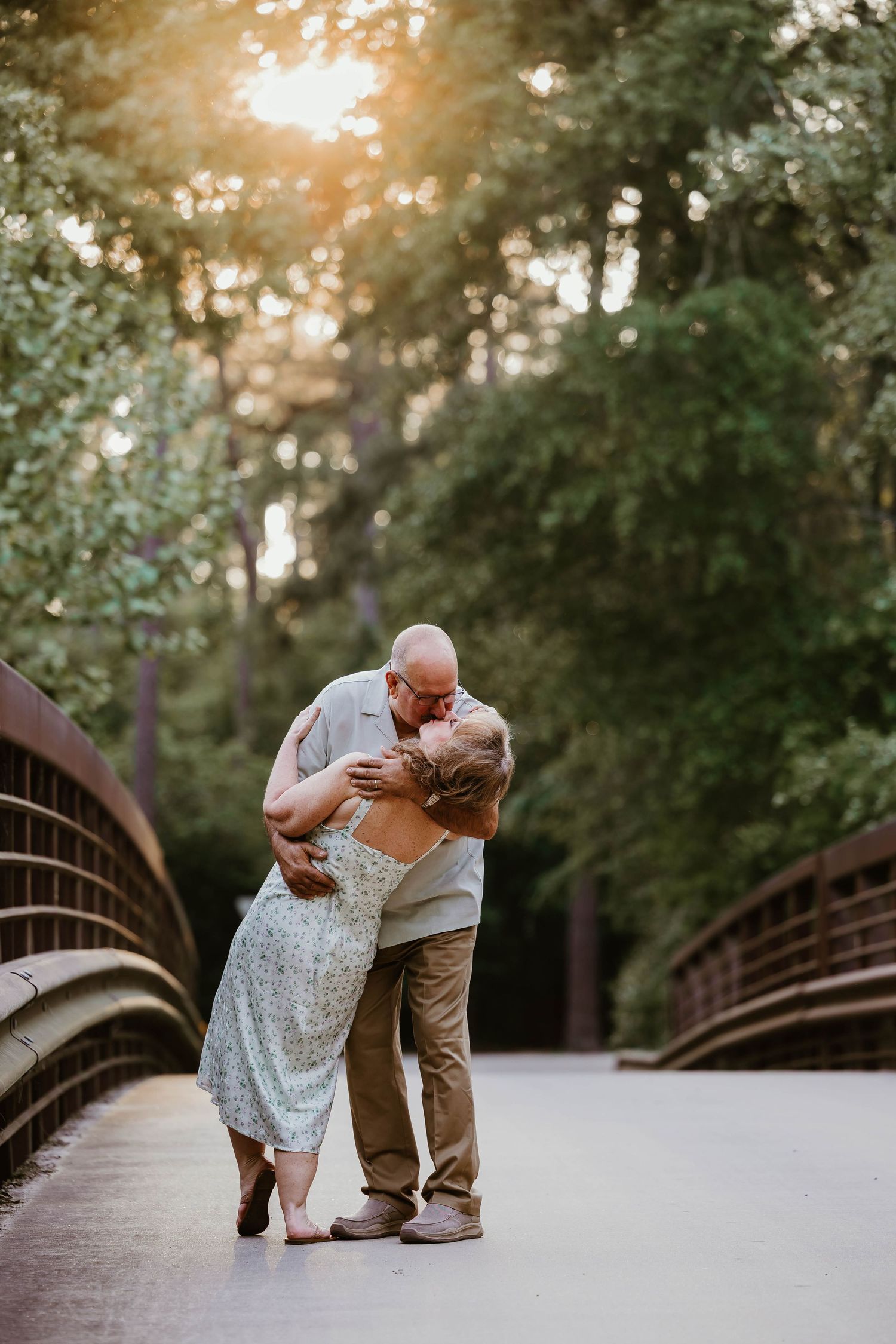 Couple sharing playful dance moves on wooden bridge at sunset.