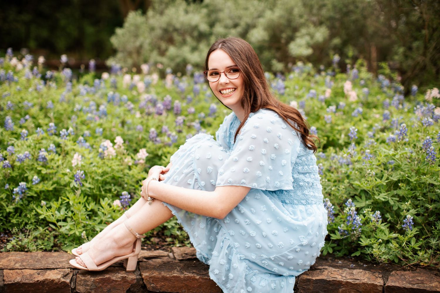 Woman in blue dress sitting among blooming wildflowers in a garden setting.