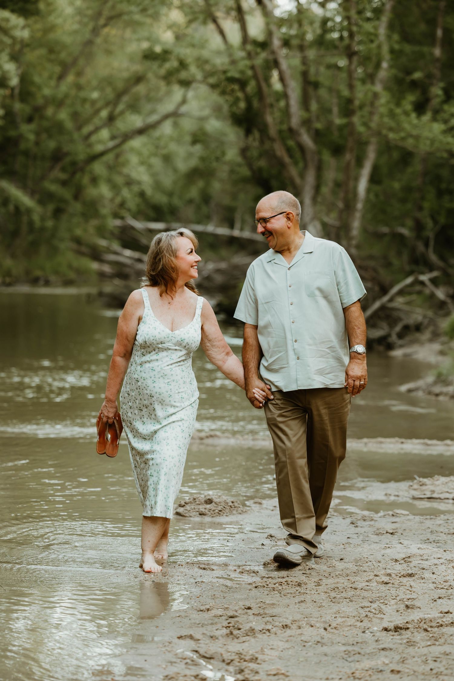 Couple walking hand in hand along a riverbank in casual summer clothing.