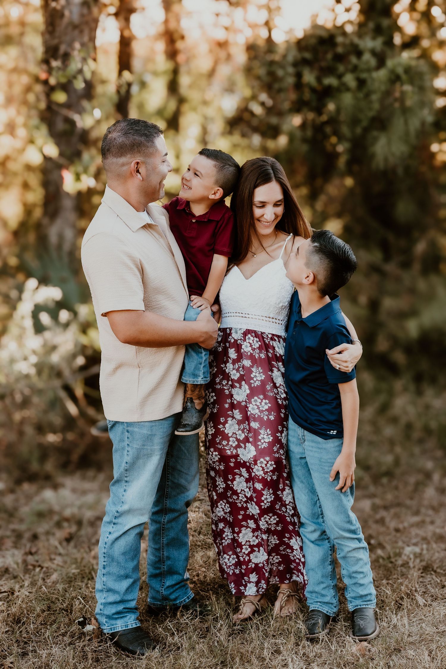 A family shares playful moments together while posing for photos in a wooded outdoor setting.