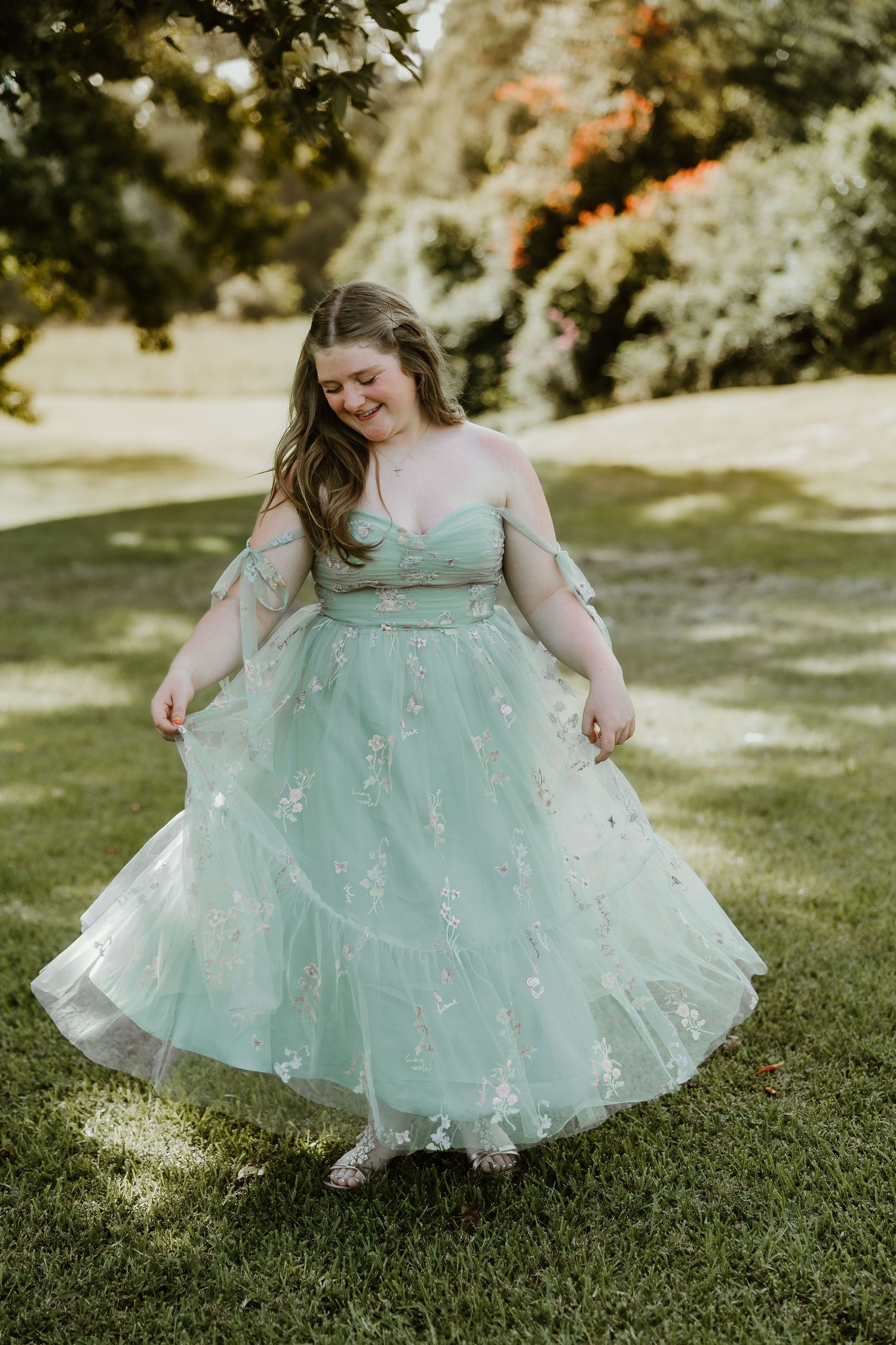Person twirling in a mint green tulle dress on sunny grass.