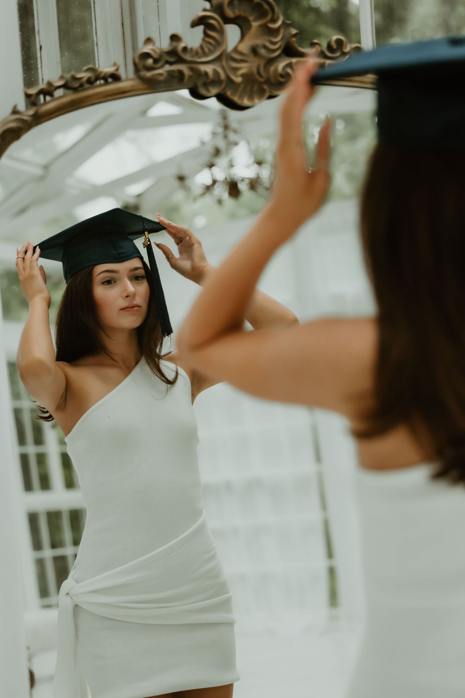 Artistic portrait session featuring a black graduation cap and white dress in front of an ornate mirror.
