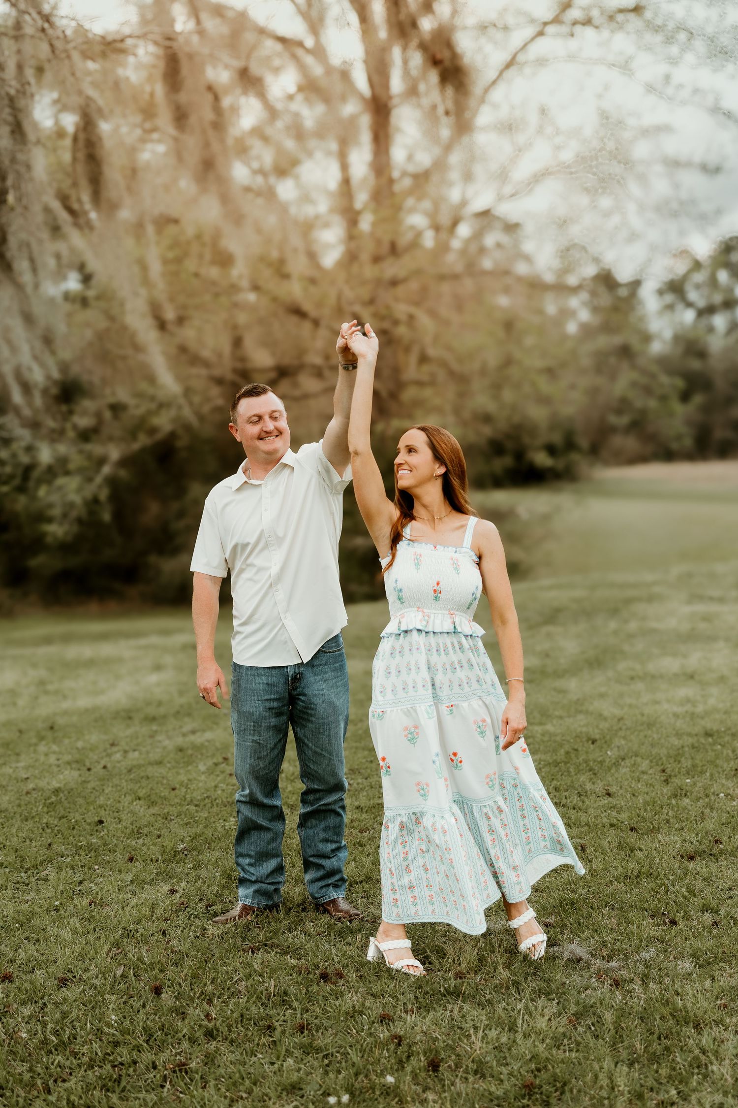 A couple dances joyfully together on a grassy hillside during a sunny spring afternoon.