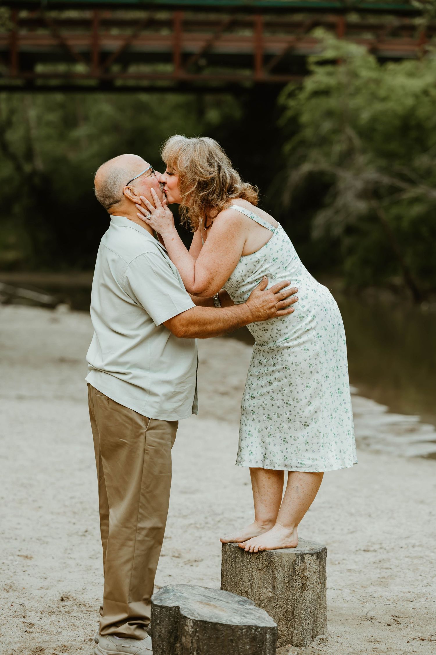 Couple sharing an intimate moment while sitting on wooden stumps by a river.