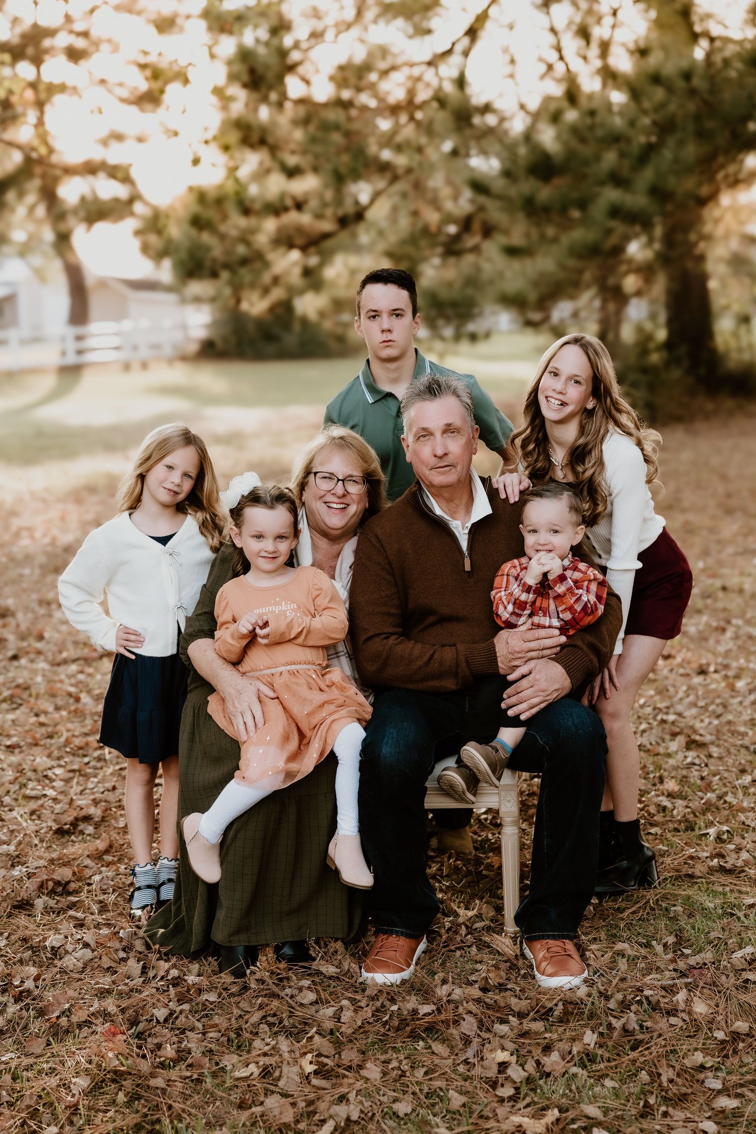 A family group sits together on fallen autumn leaves during an outdoor photo session.