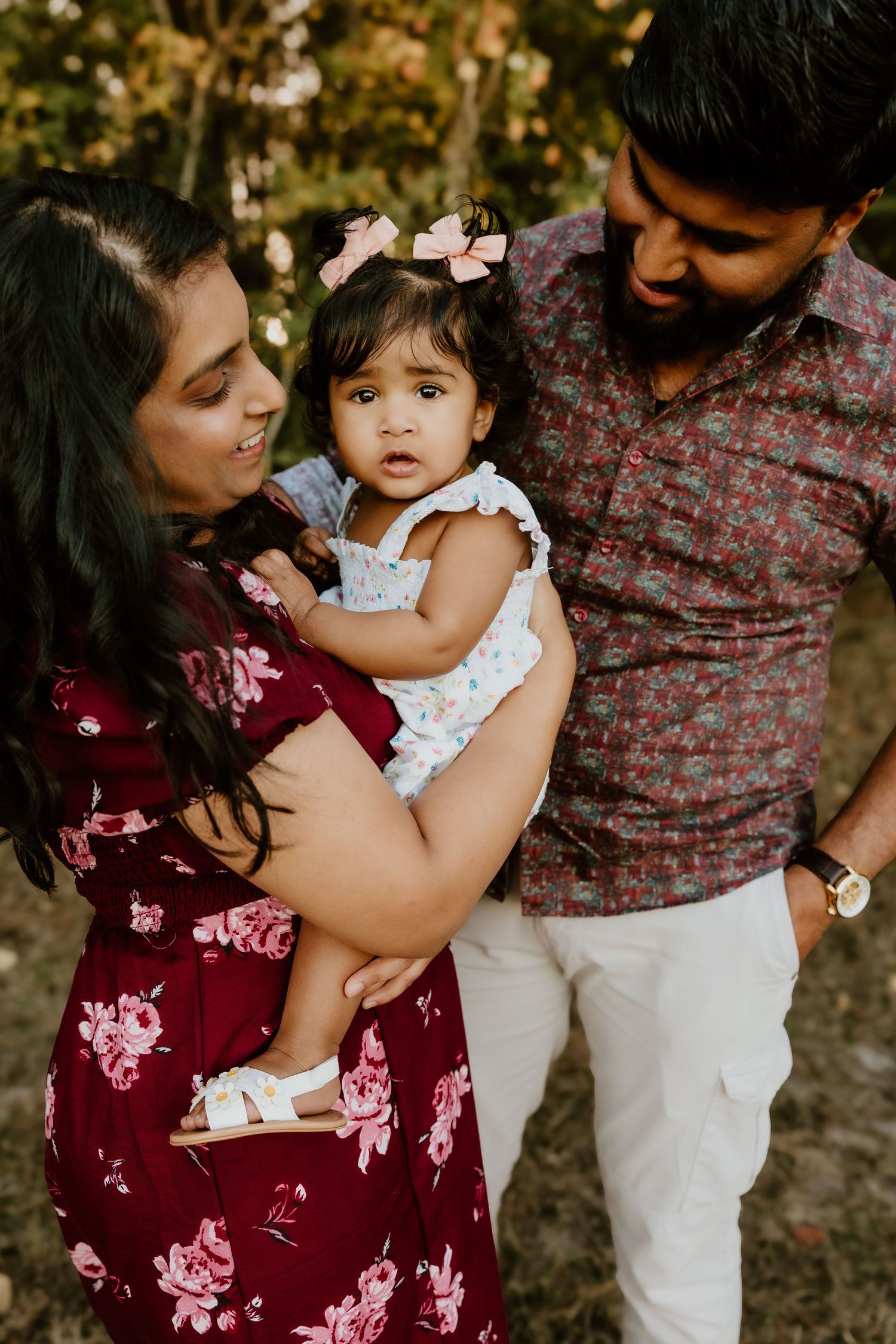 A family shares tender moments together outdoors during a photo session wearing burgundy and white outfits.
