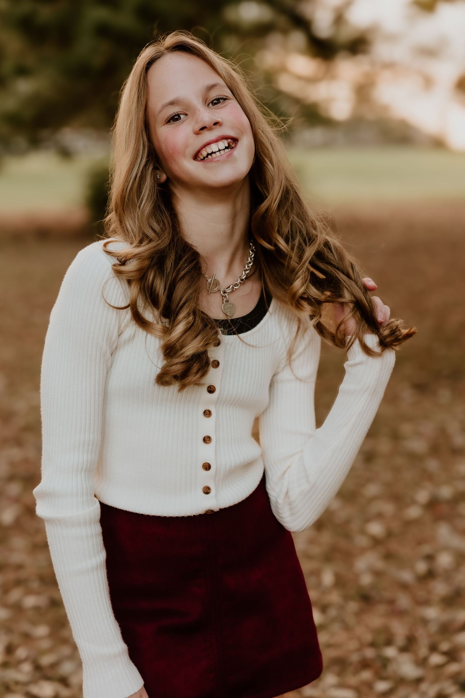 Outdoor portrait of someone wearing a white ribbed cardigan and burgundy skirt in warm autumn lighting.