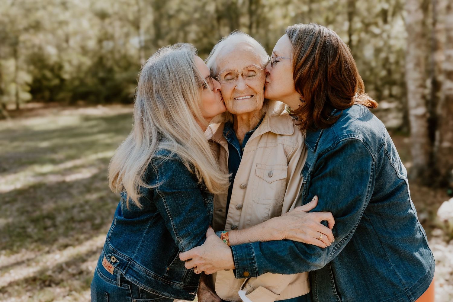 Three generations of family members share loving embraces and kisses outdoors in warm sunlight.