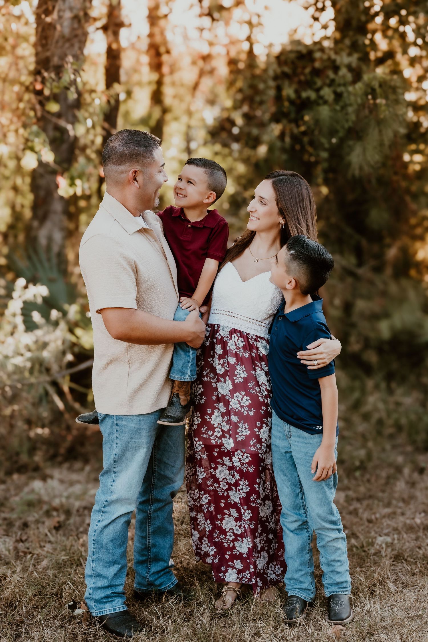 A family poses together outdoors in coordinated outfits during golden hour sunset in a wooded setting.