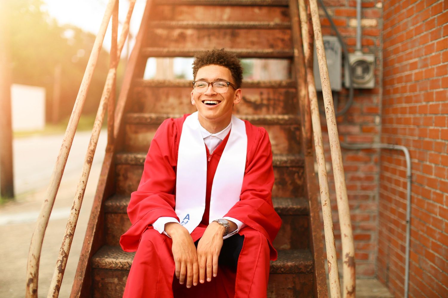 Person in red blazer posing against rustic brick wall with warm lighting.