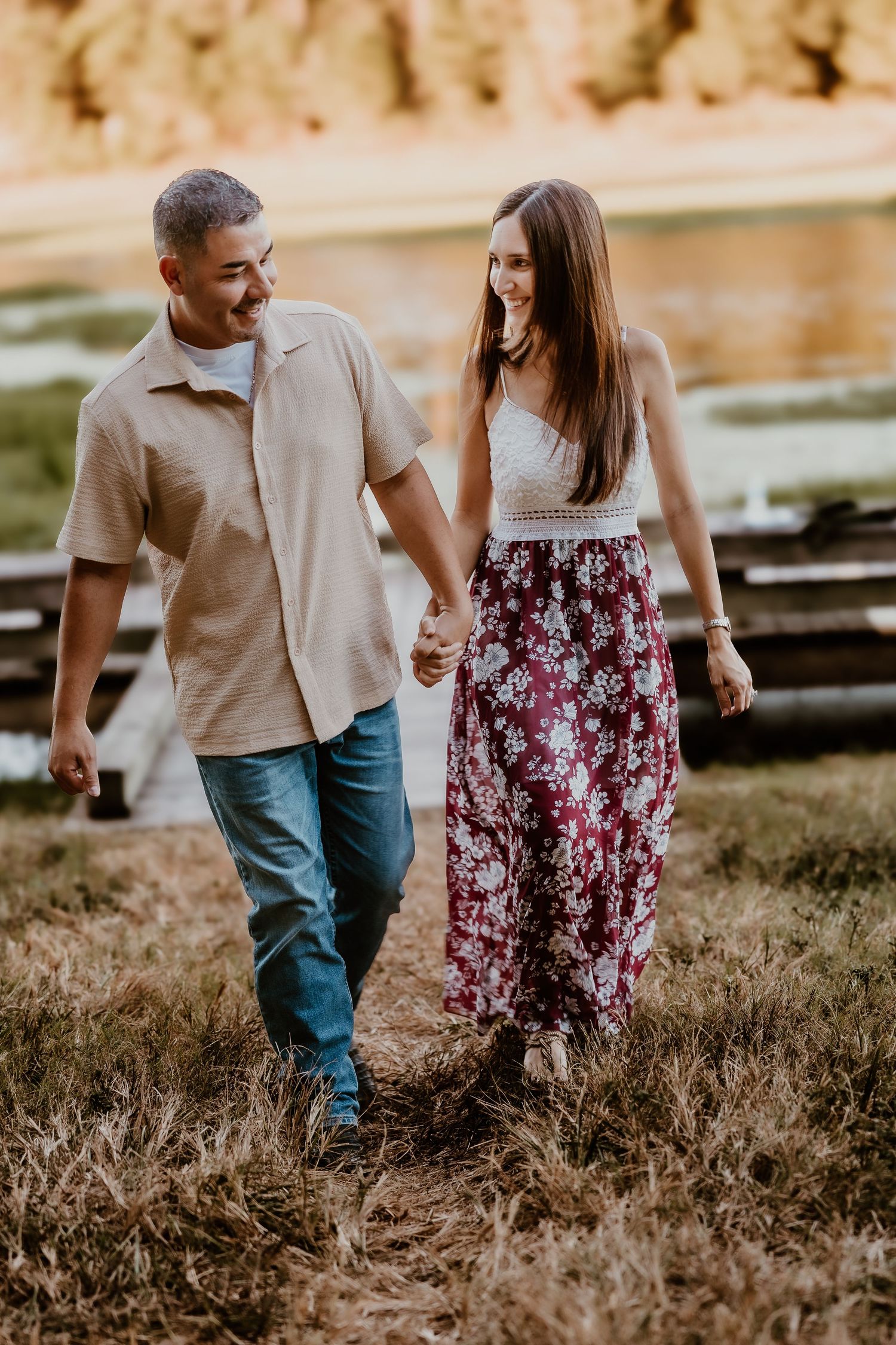Couple walking hand in hand through golden field at sunset.