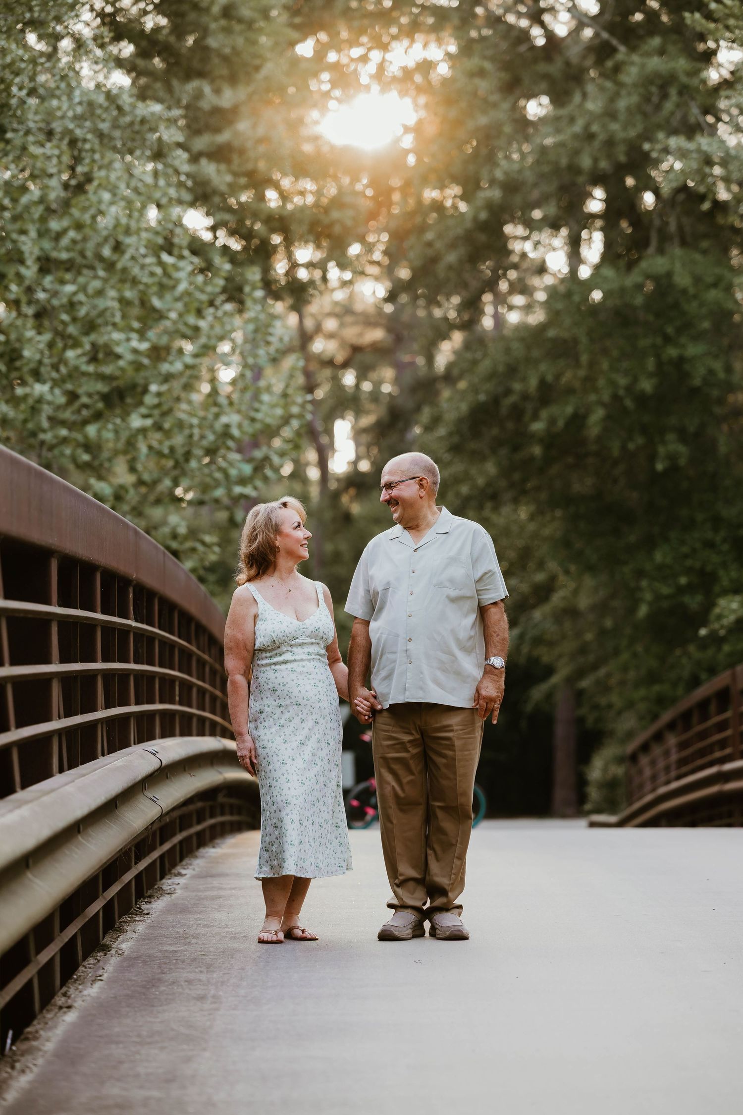 Couple walking hand in hand across wooden bridge during golden hour.