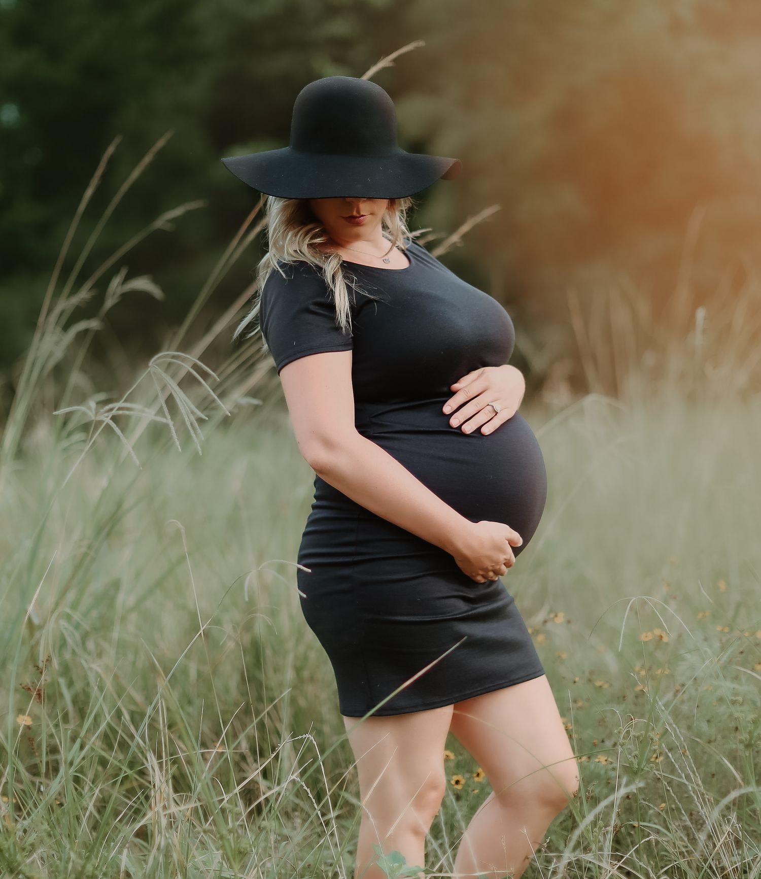Maternity photos showing a black dress silhouette against tall grass at sunset.