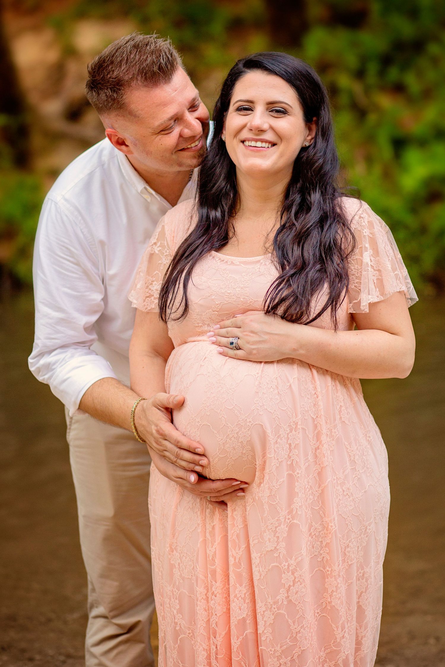 A couple embraces lovingly while wearing peach and khaki colored outfits in an outdoor setting.