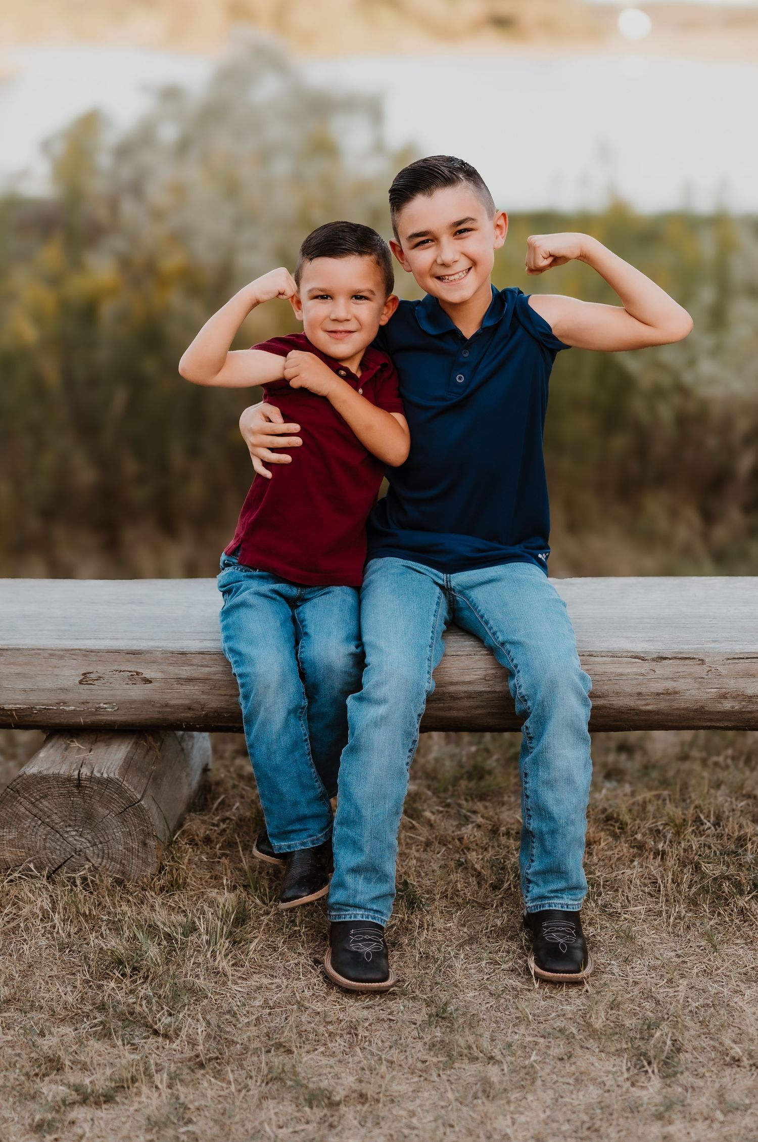 Two boys in casual wear showing off their muscles while sitting on a wooden beam.