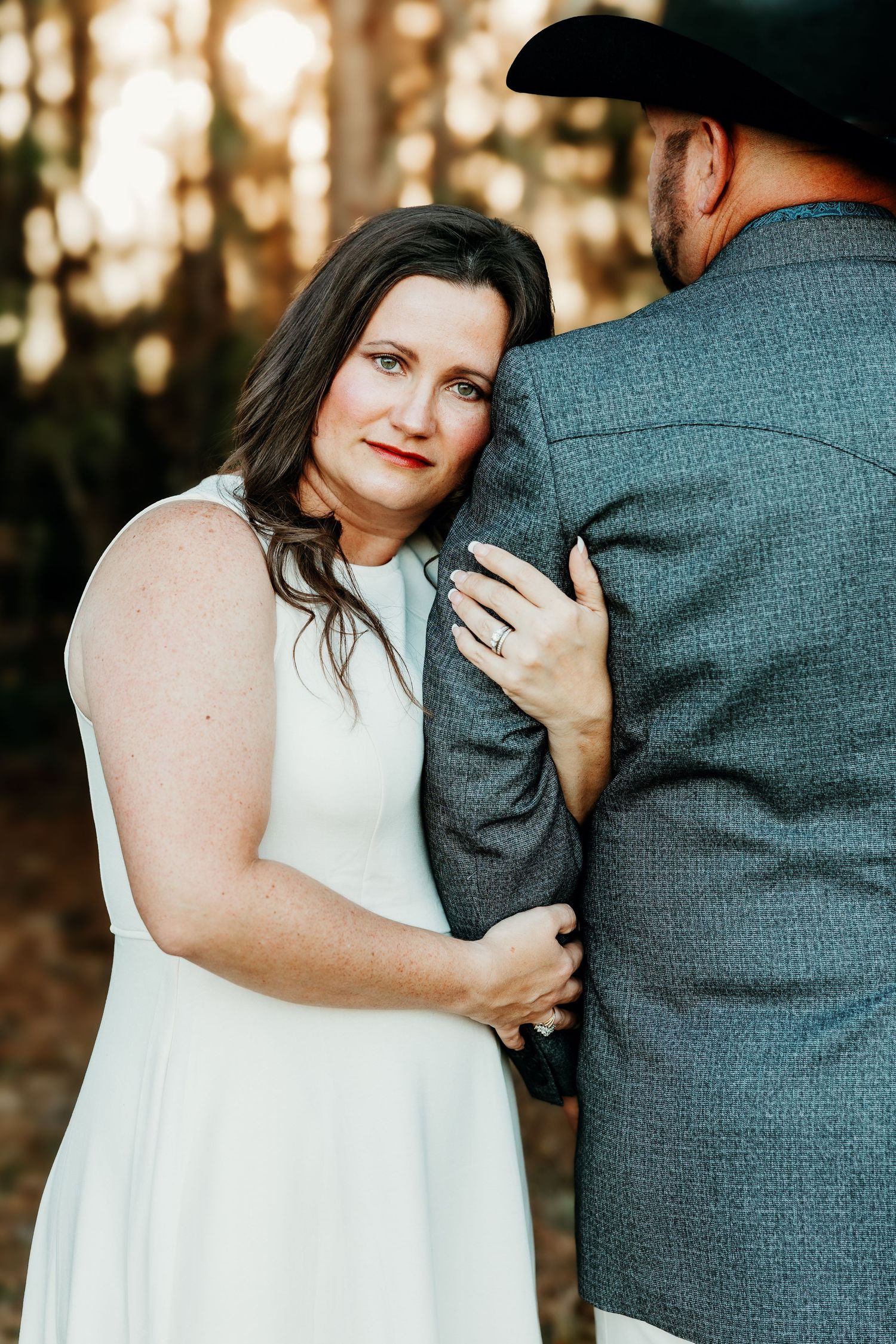 Romantic outdoor engagement photos show couple embracing in white dress and gray sweater at sunset.