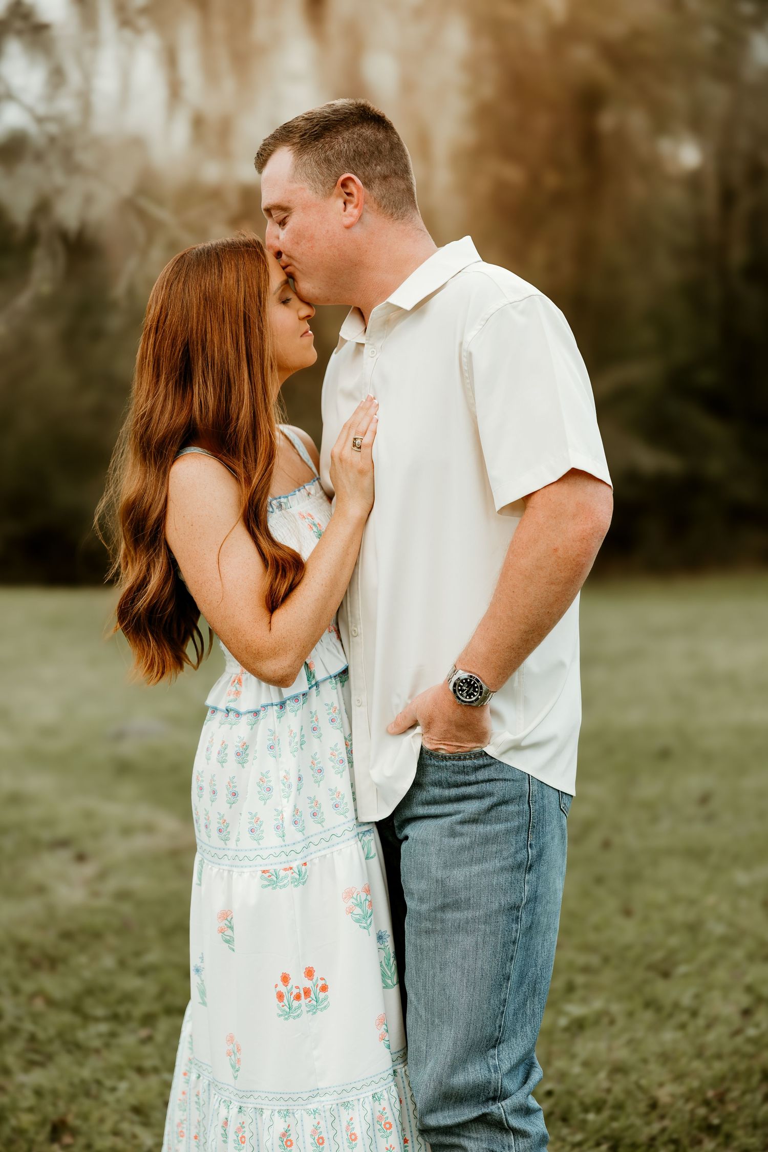 A couple shares romantic kisses in a grassy field wearing casual spring outfits in a series of intimate portraits.
