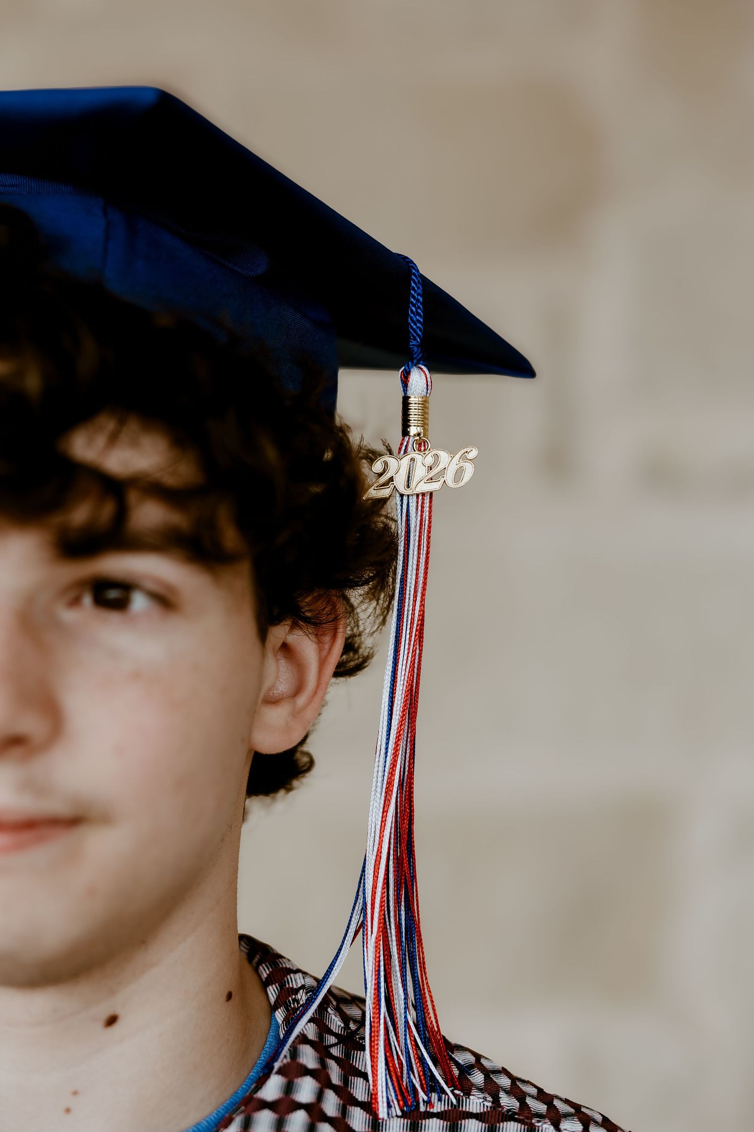 Young man wearing a navy blue 2026 graduation cap with red, white, and blue tassel, smiling confidently.