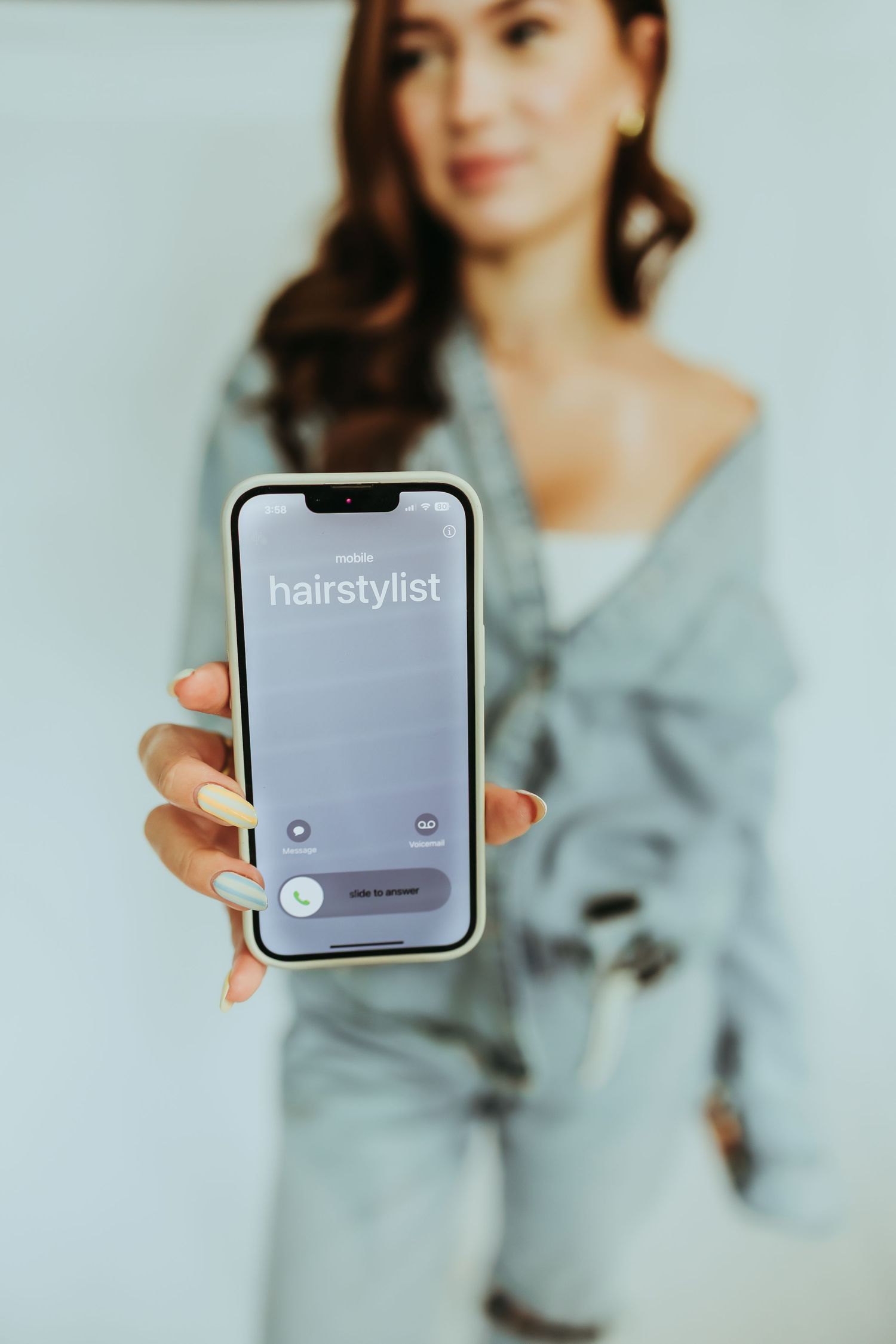 Hand holding smartphone displaying hairstylist app against blurred background.
