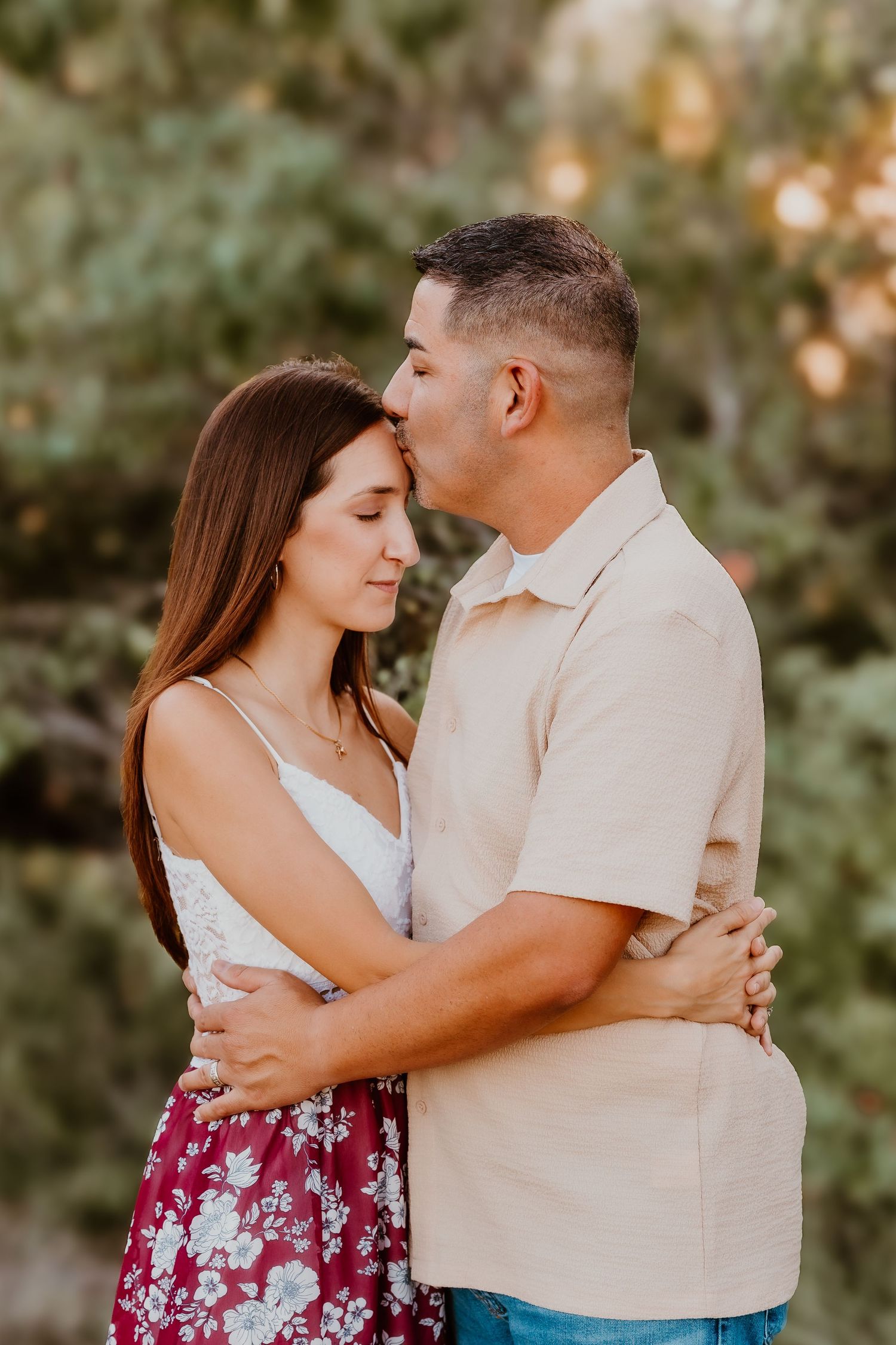 Romantic couple embracing in a park during golden hour wearing casual summer attire.