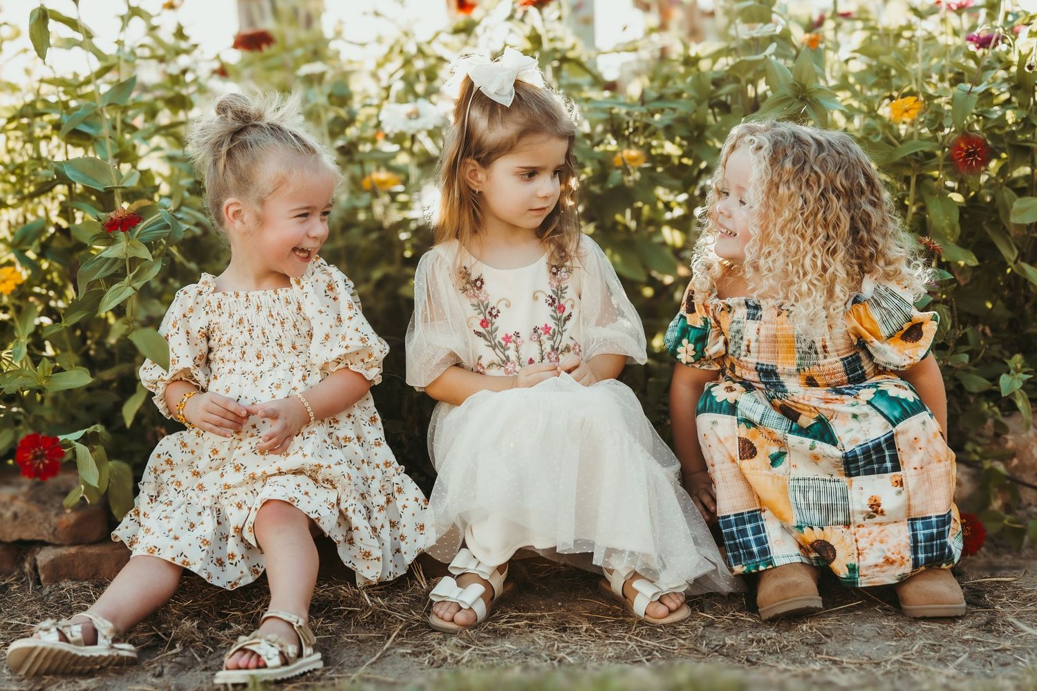 Children sitting among autumn decorations and plush toys in garden setting.