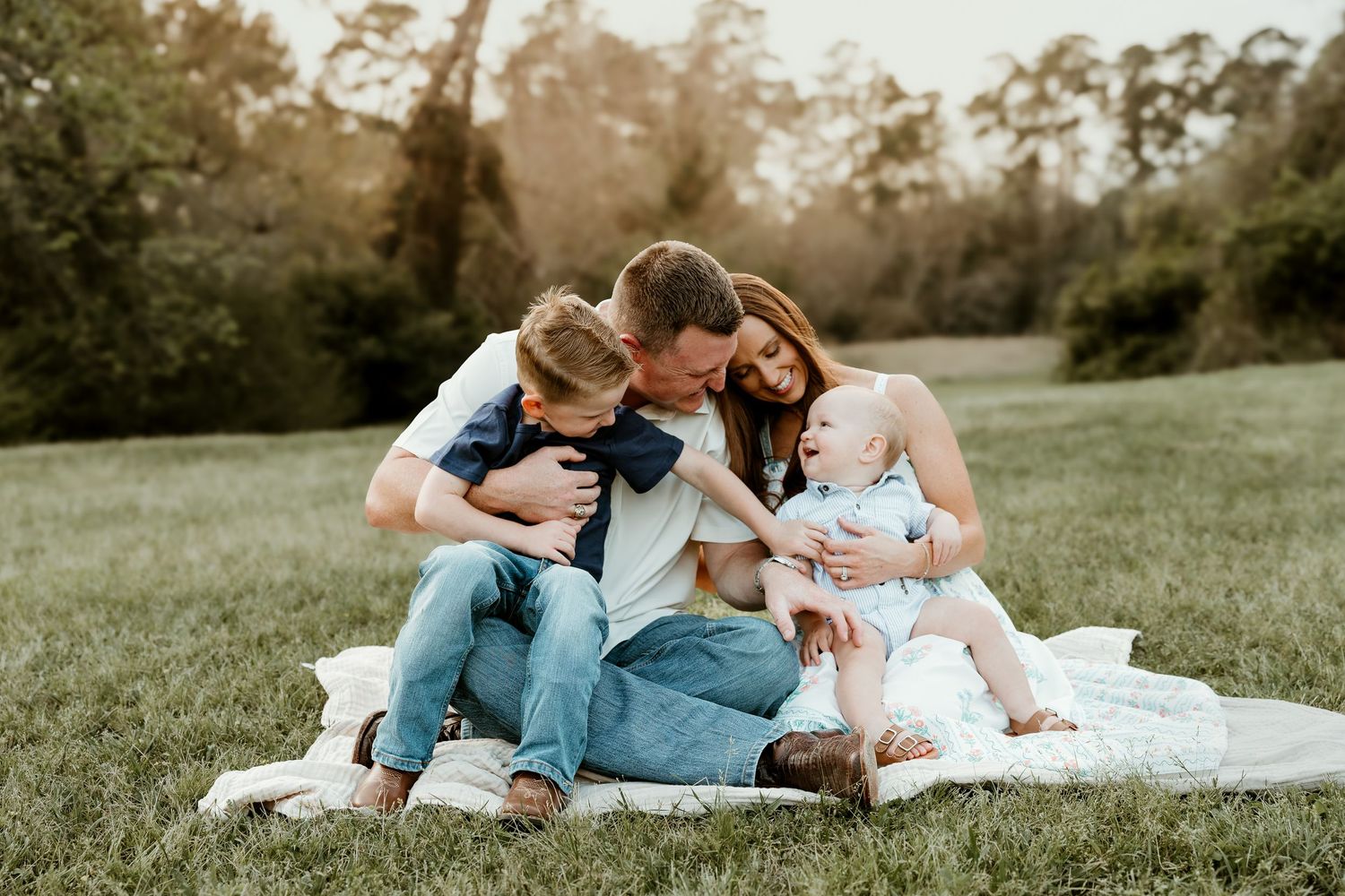 Family enjoying quality time together on a white blanket in a grassy field during golden hour.