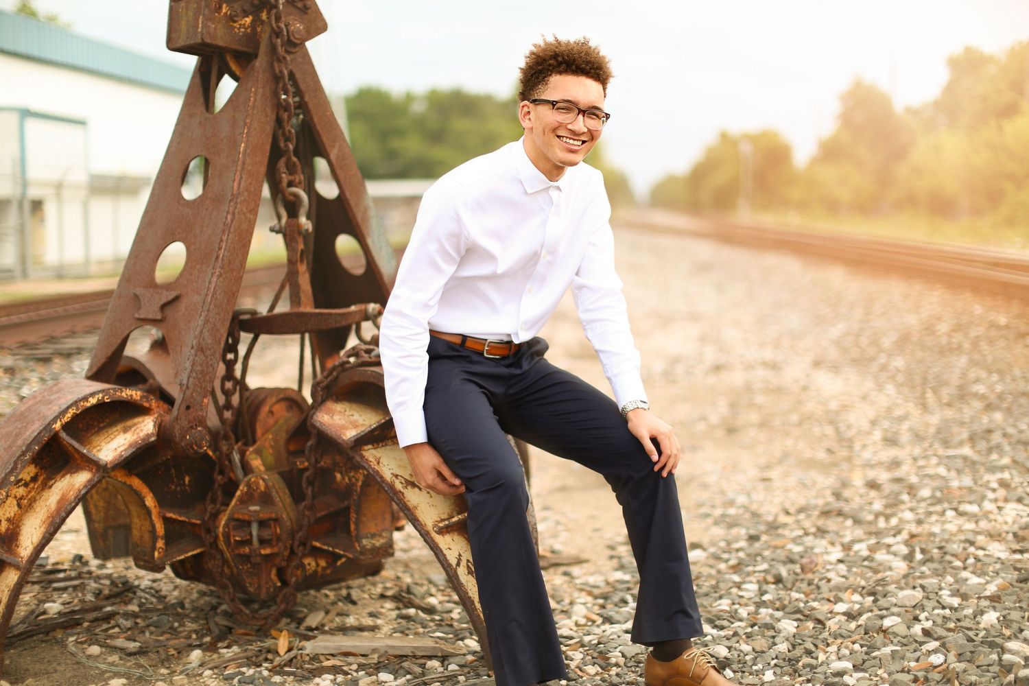 Person in white shirt and glasses sitting on vintage industrial equipment at sunset.
