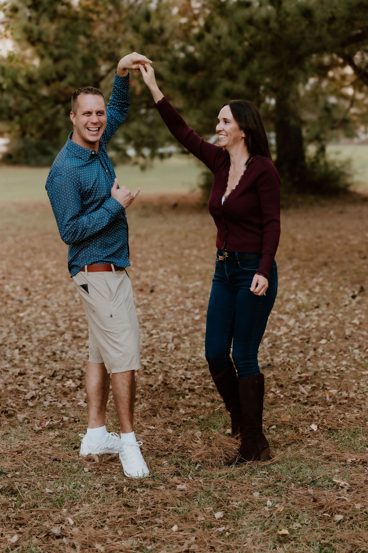A couple dances playfully together on fallen autumn leaves in a park setting.