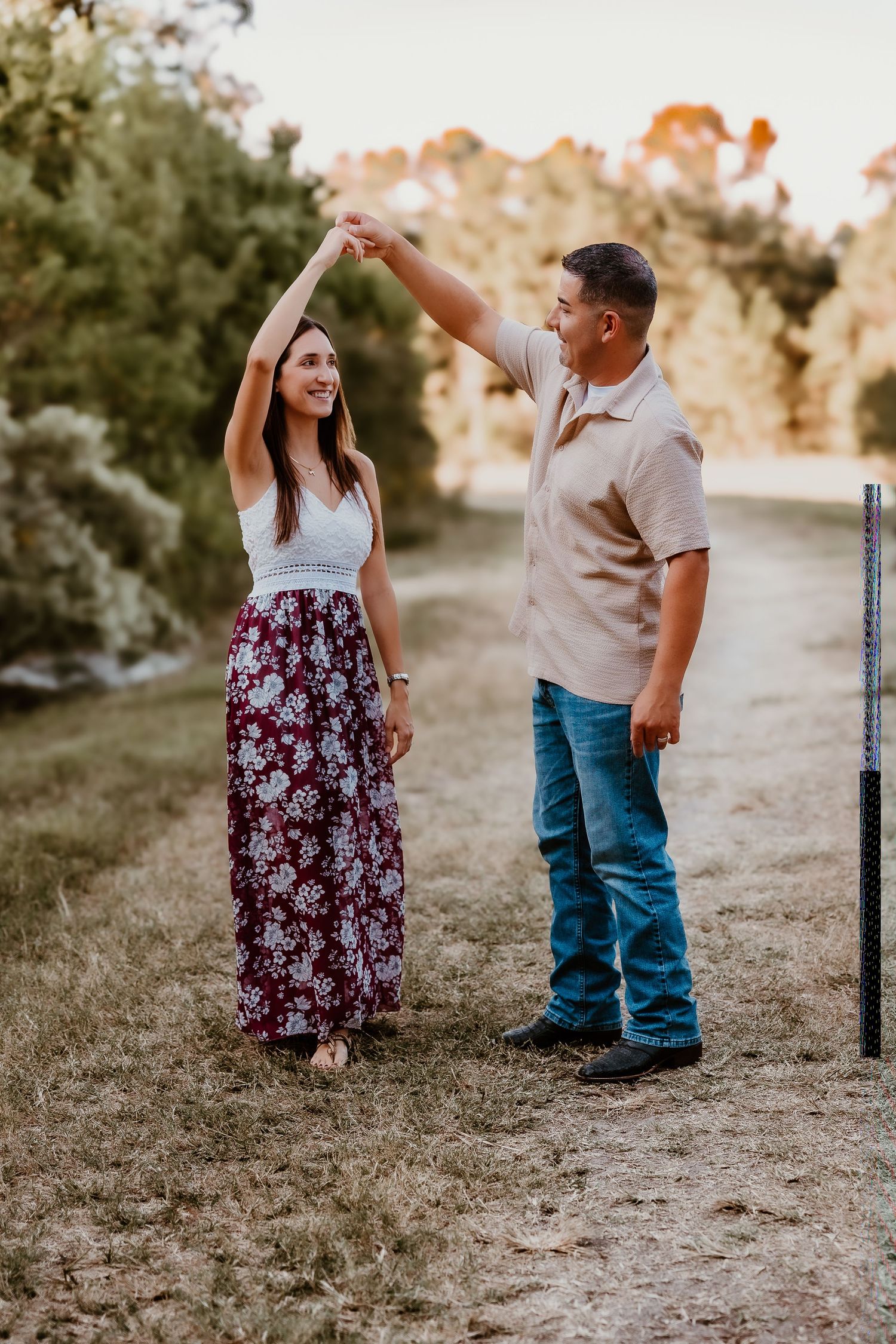 Couple in casual attire walking together on a dirt path during sunset.