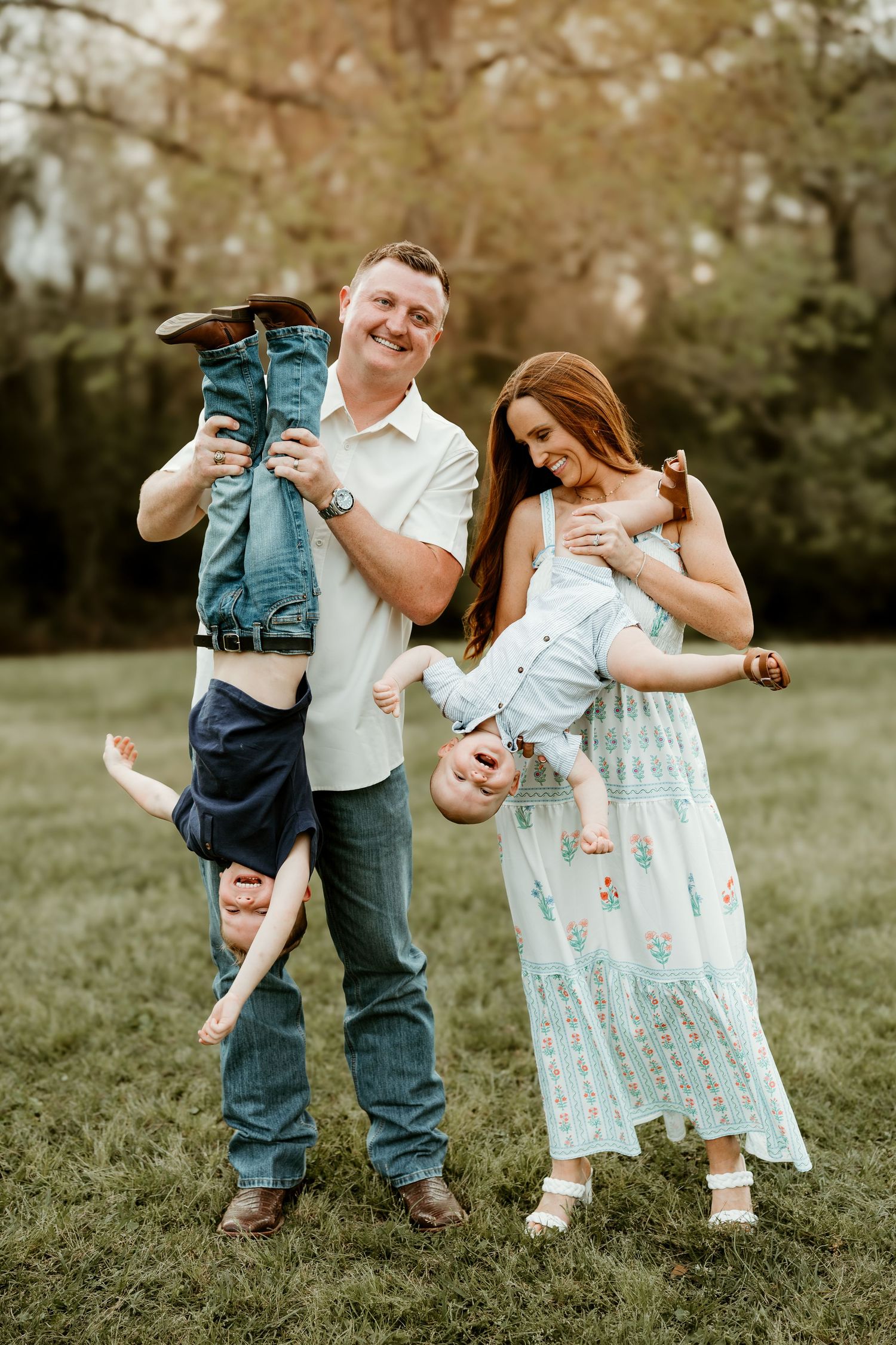 A family in coordinating outfits plays together on grass during a casual outdoor photo session.