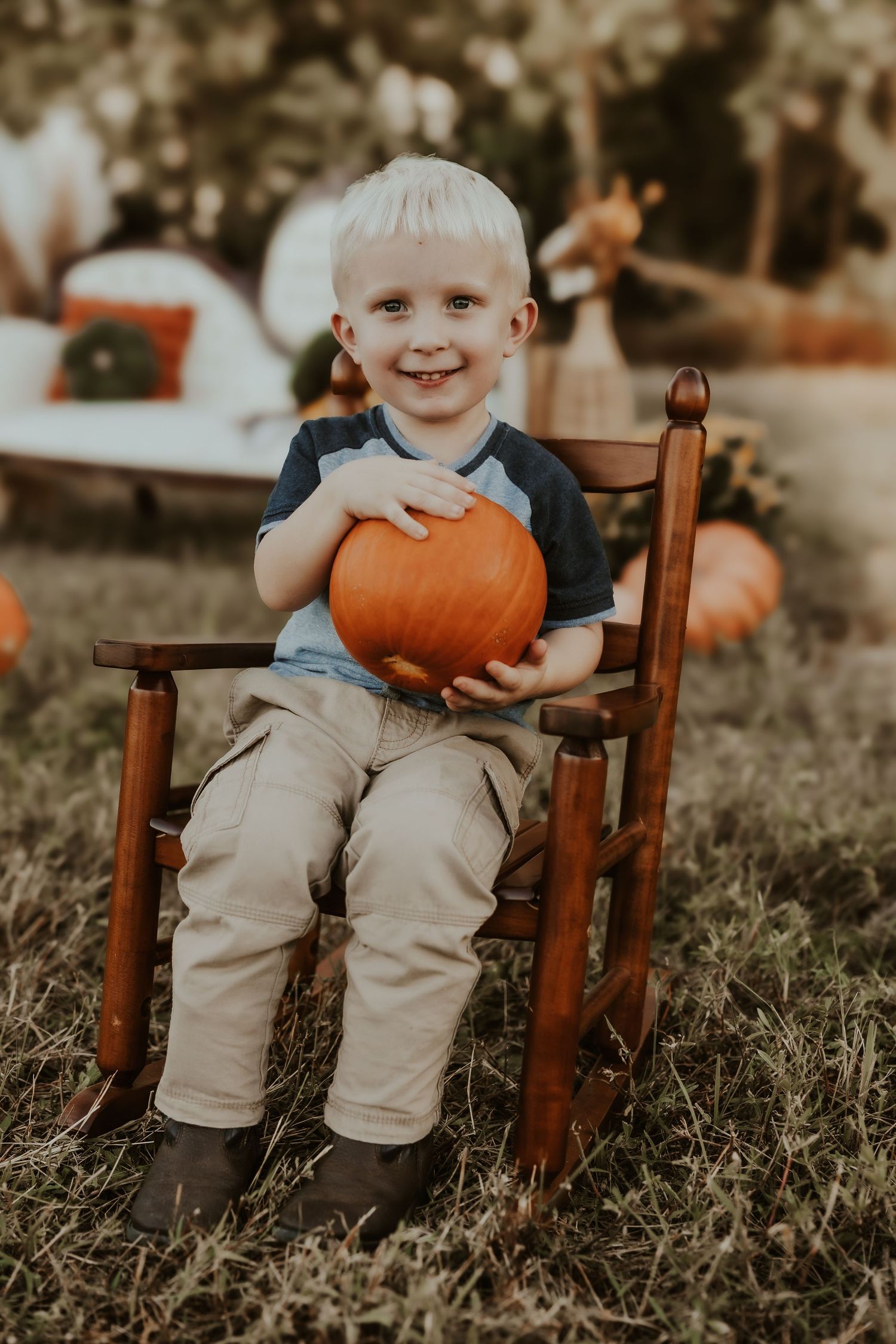 Child sitting in wooden chair with orange pumpkin during fall photoshoot.