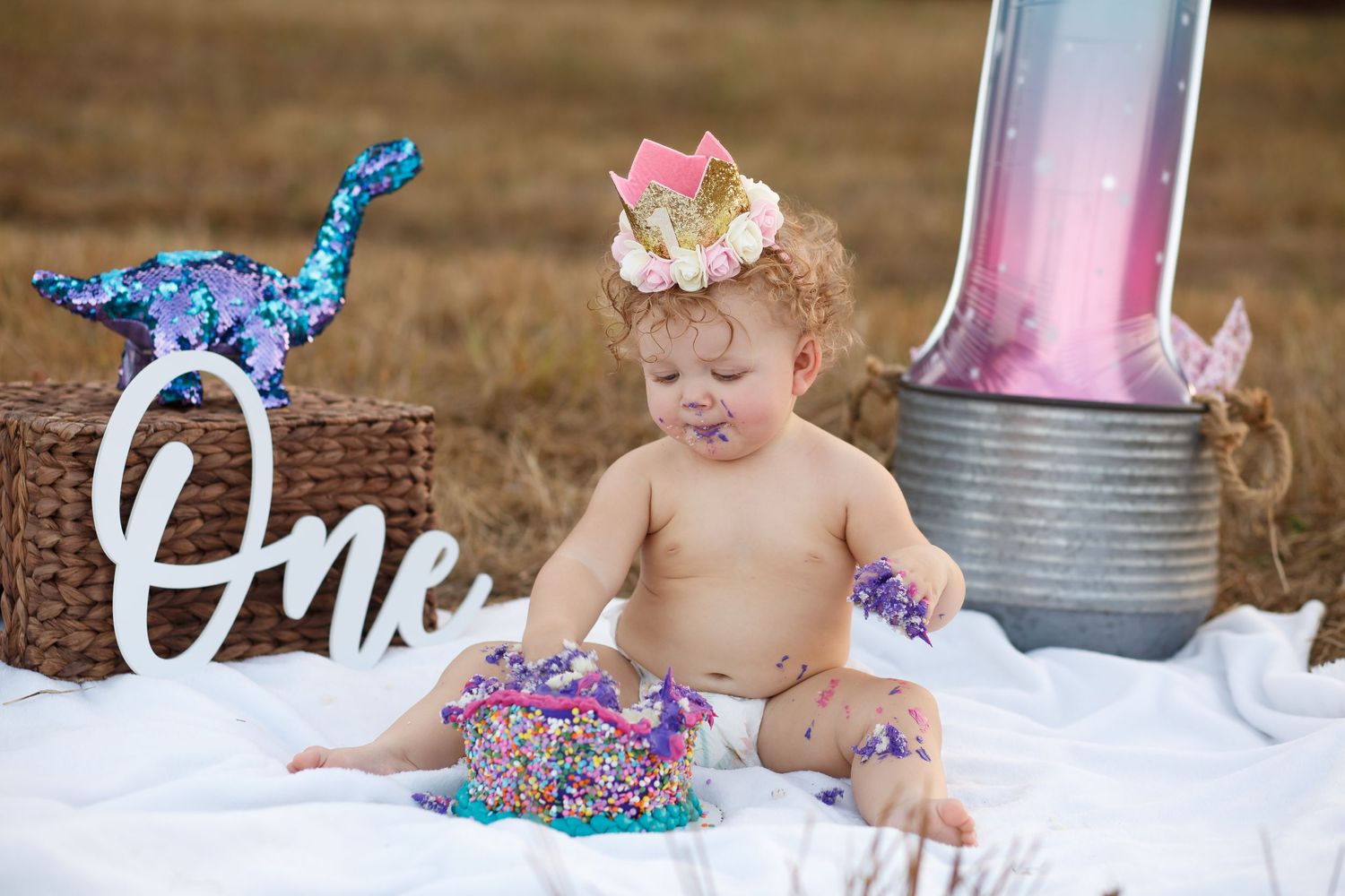 Baby in sparkly tutu dress sits on white blanket with rustic decor.