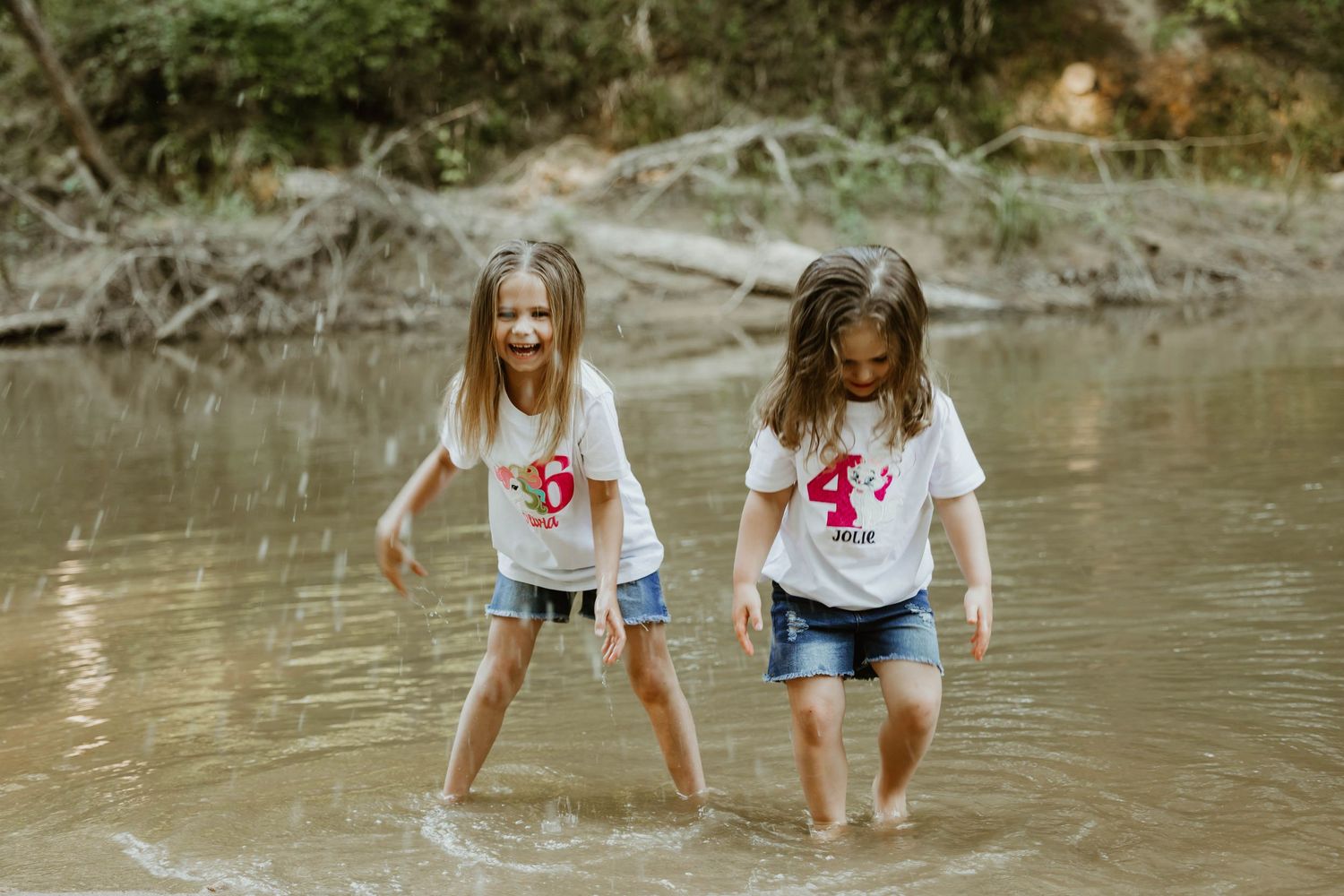 Children play and splash in the muddy shallows of a creek on a warm day.