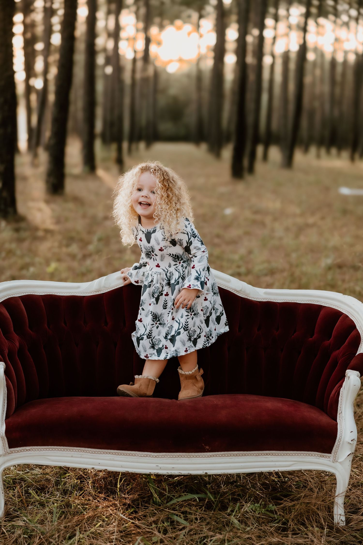 A vintage burgundy velvet sofa sits in a serene forest setting during golden hour.