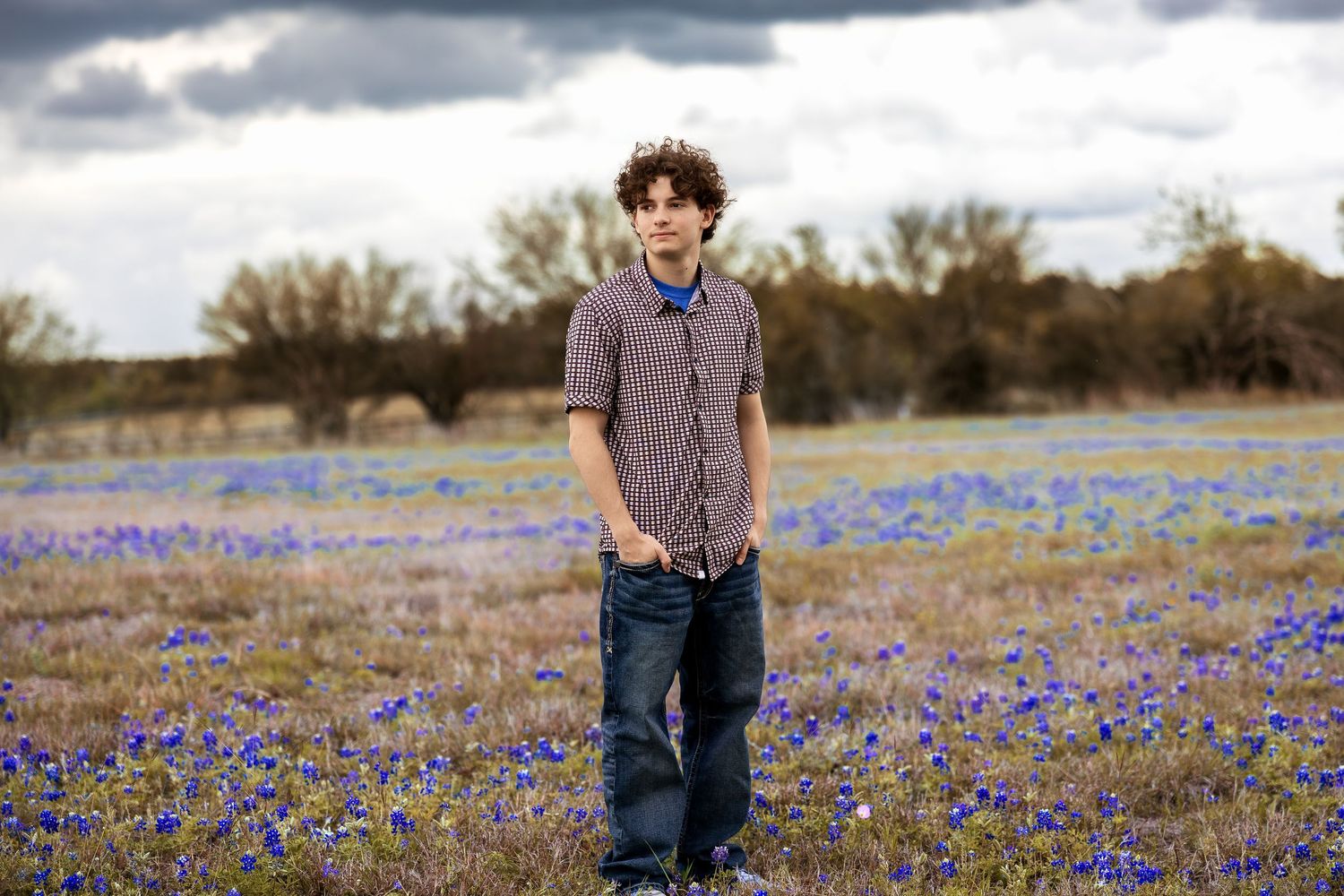 Teen boy standing in a field of blue wildflowers under cloudy skies in a rural Texas landscape.
