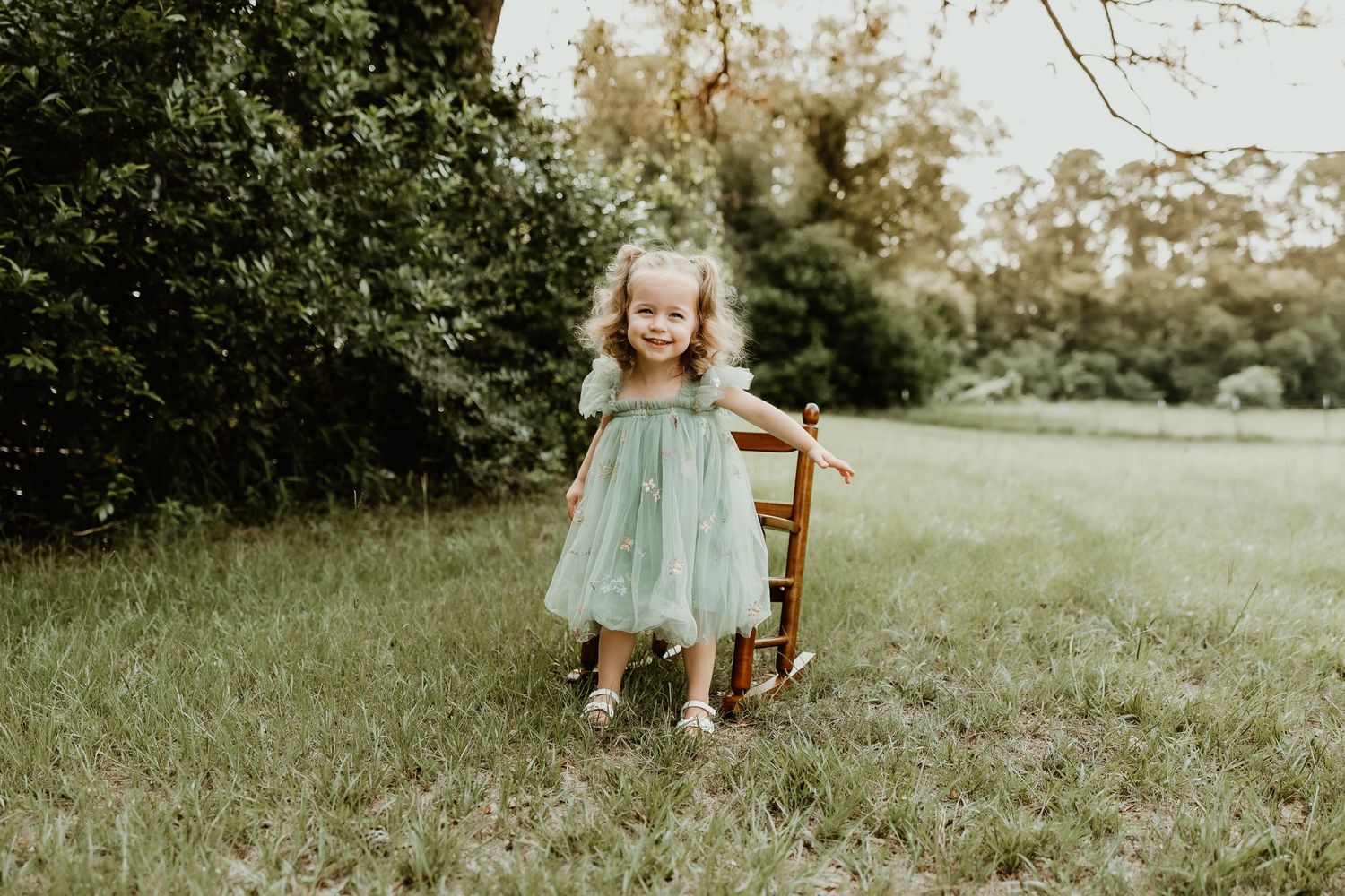 Child playing in a grassy field wearing mint green clothing.