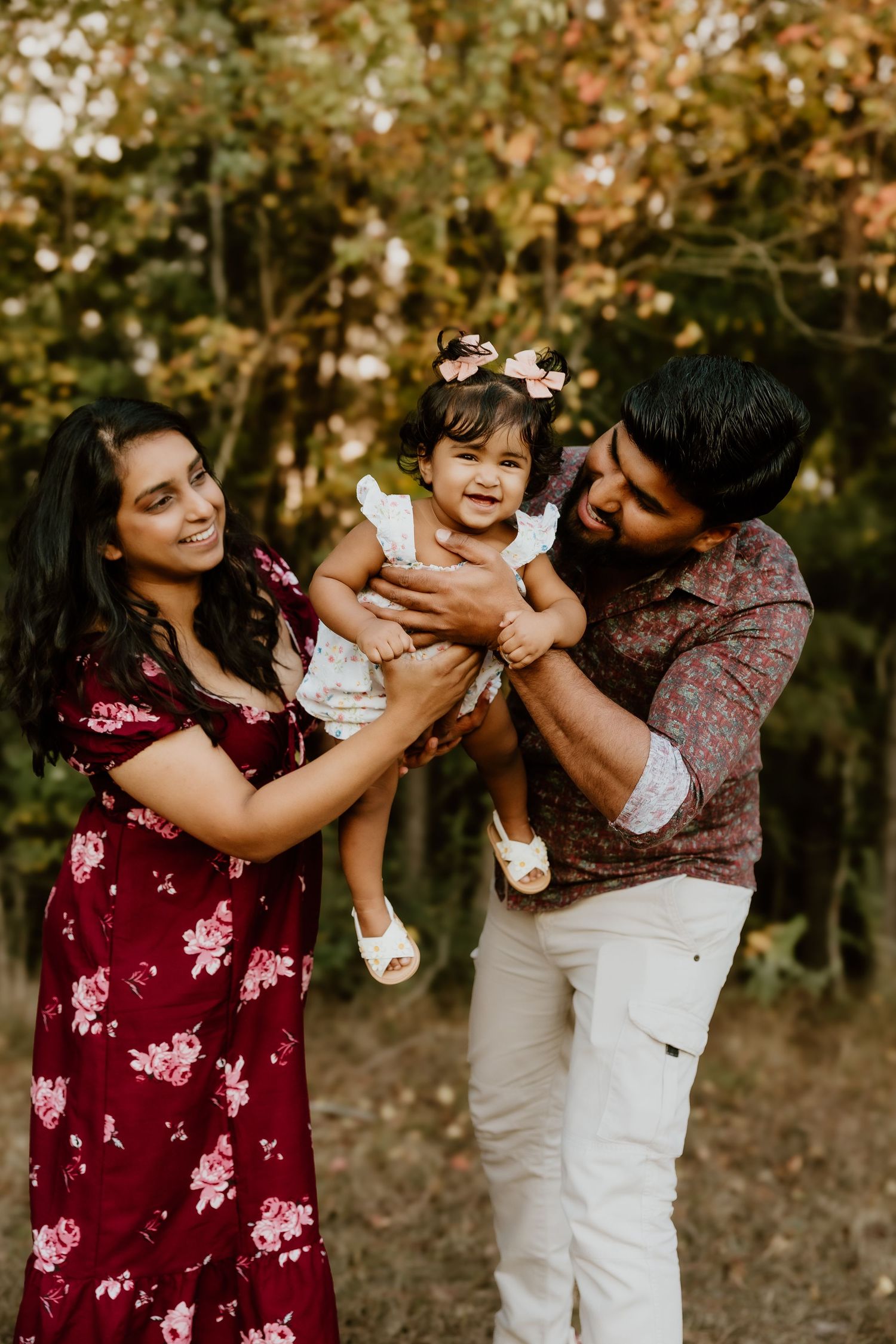 A family shares playful moments together in a wooded setting during golden hour, wearing burgundy and white outfits.